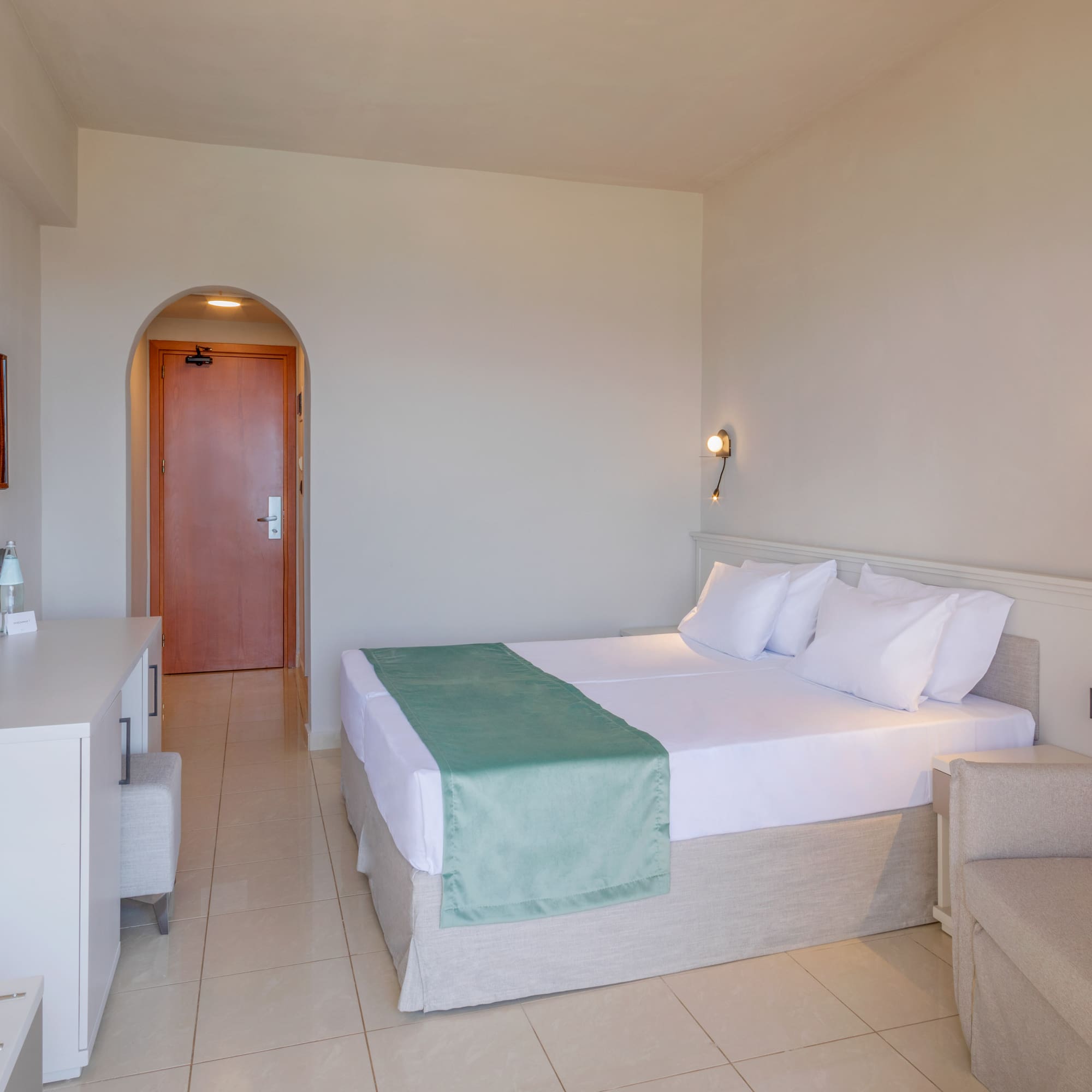 Modern hotel room with twin beds, green runner, TV, and lounge area.