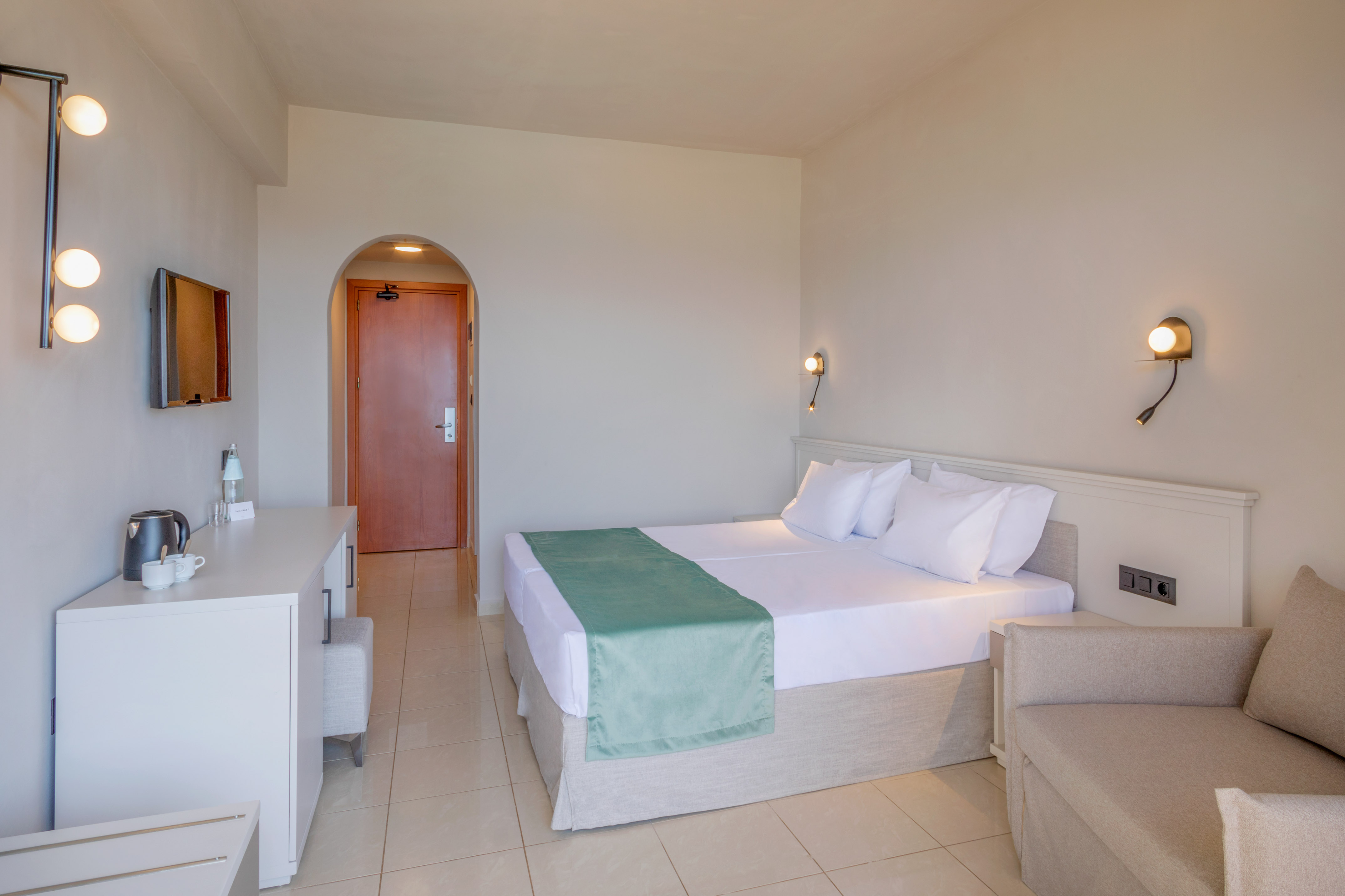 Modern hotel room with twin beds, green runner, TV, and lounge area.