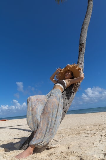 a woman leaning against a tree on a beach