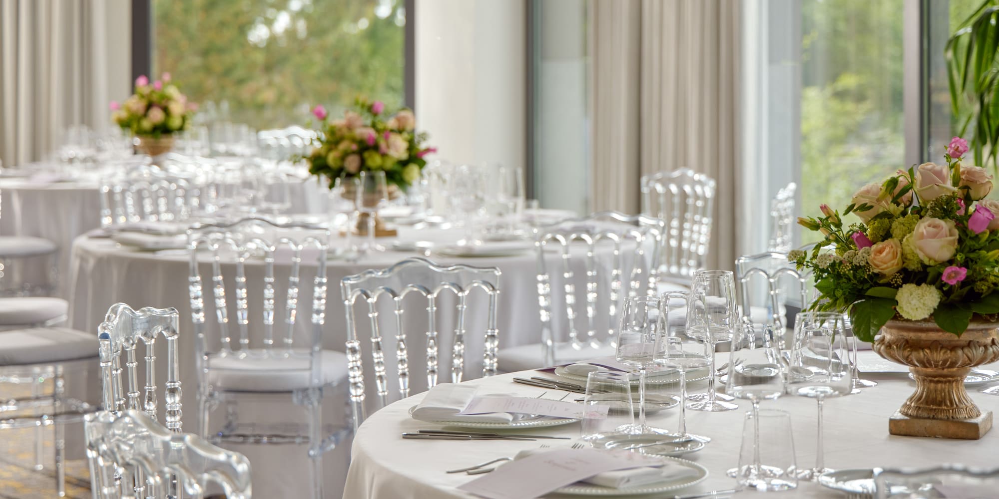 Elegant banquet hall set with white tables, clear chairs, and floral centerpieces.