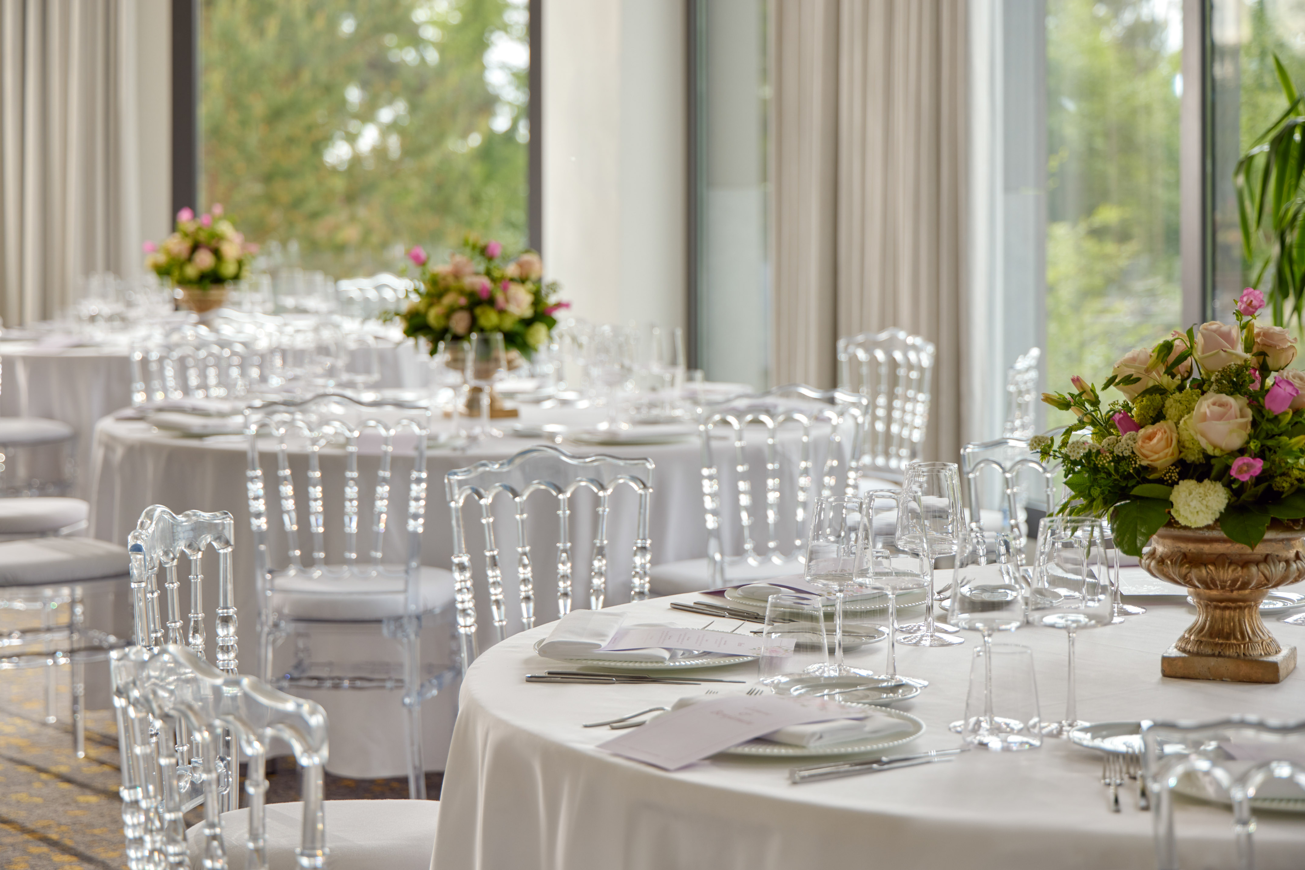 Elegant banquet hall set with white tables, clear chairs, and floral centerpieces.