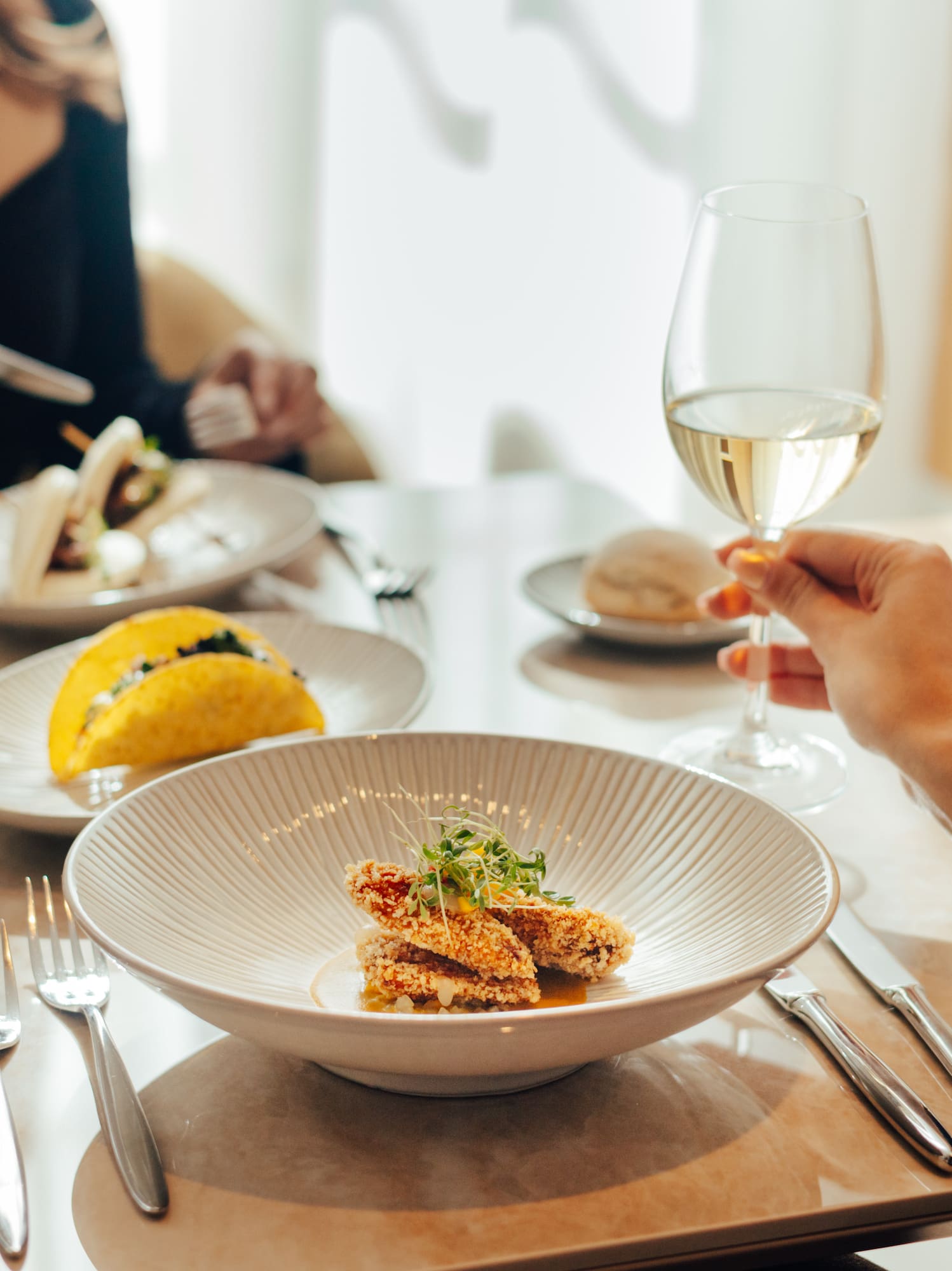 Fine dining setting with gourmet appetizers, tacos, bread, and white wine.