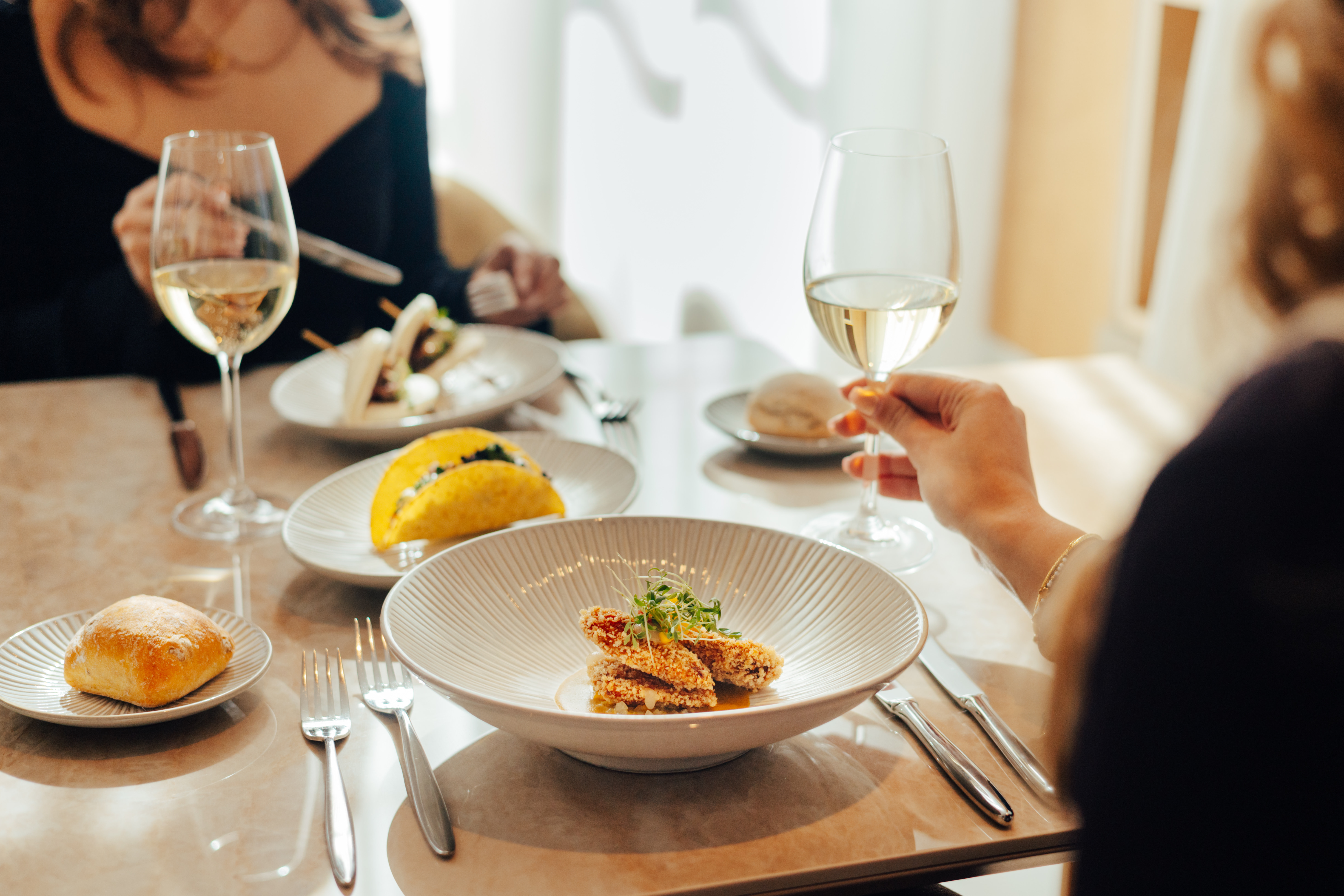 Fine dining setting with gourmet appetizers, tacos, bread, and white wine.