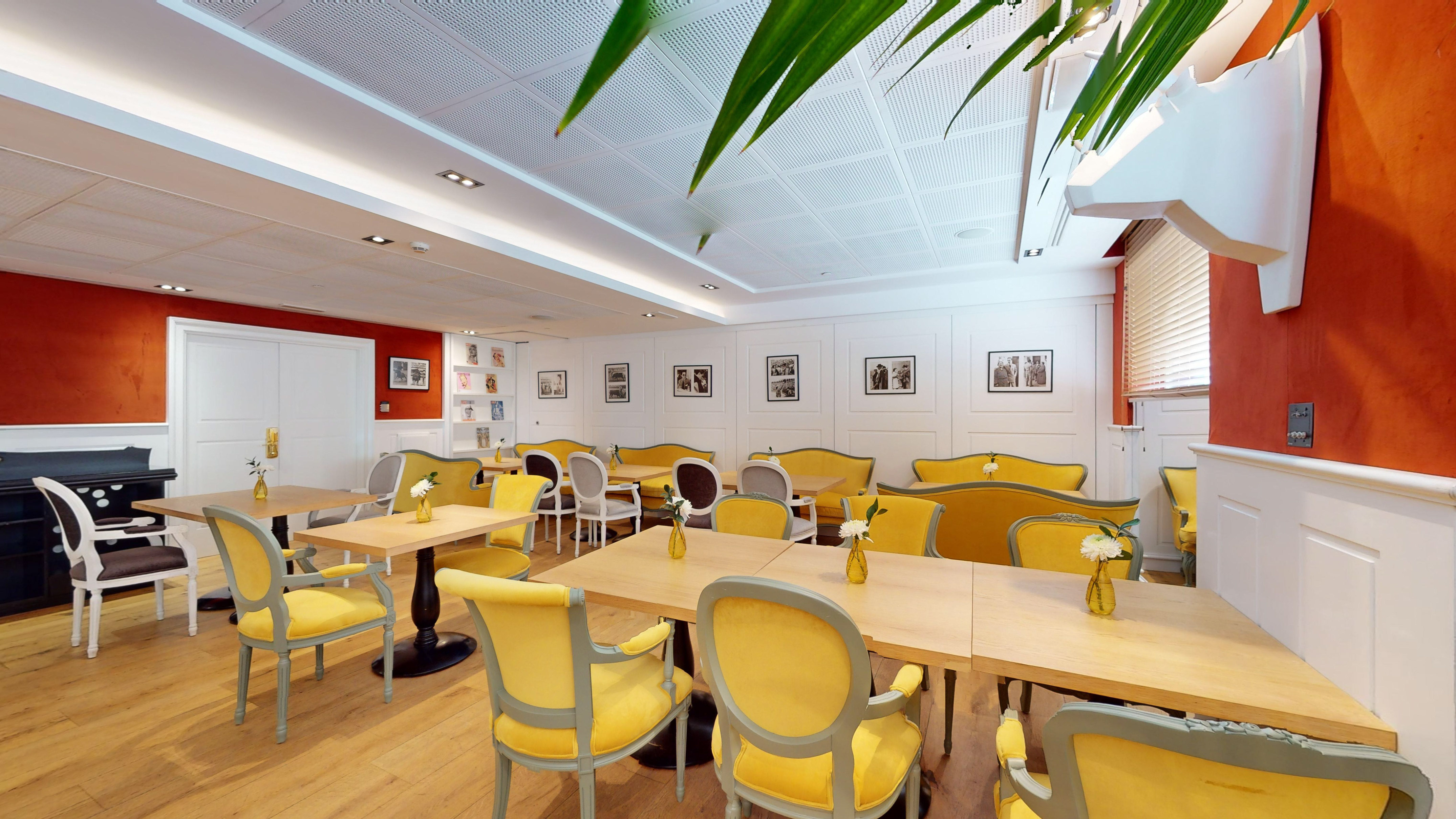 Elegant cafe dining room with yellow velvet chairs, wooden tables, and orange walls.