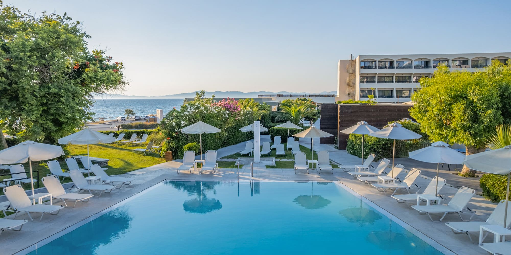 Resort hotel pool, sun loungers, umbrellas, ocean view, and lush gardens.