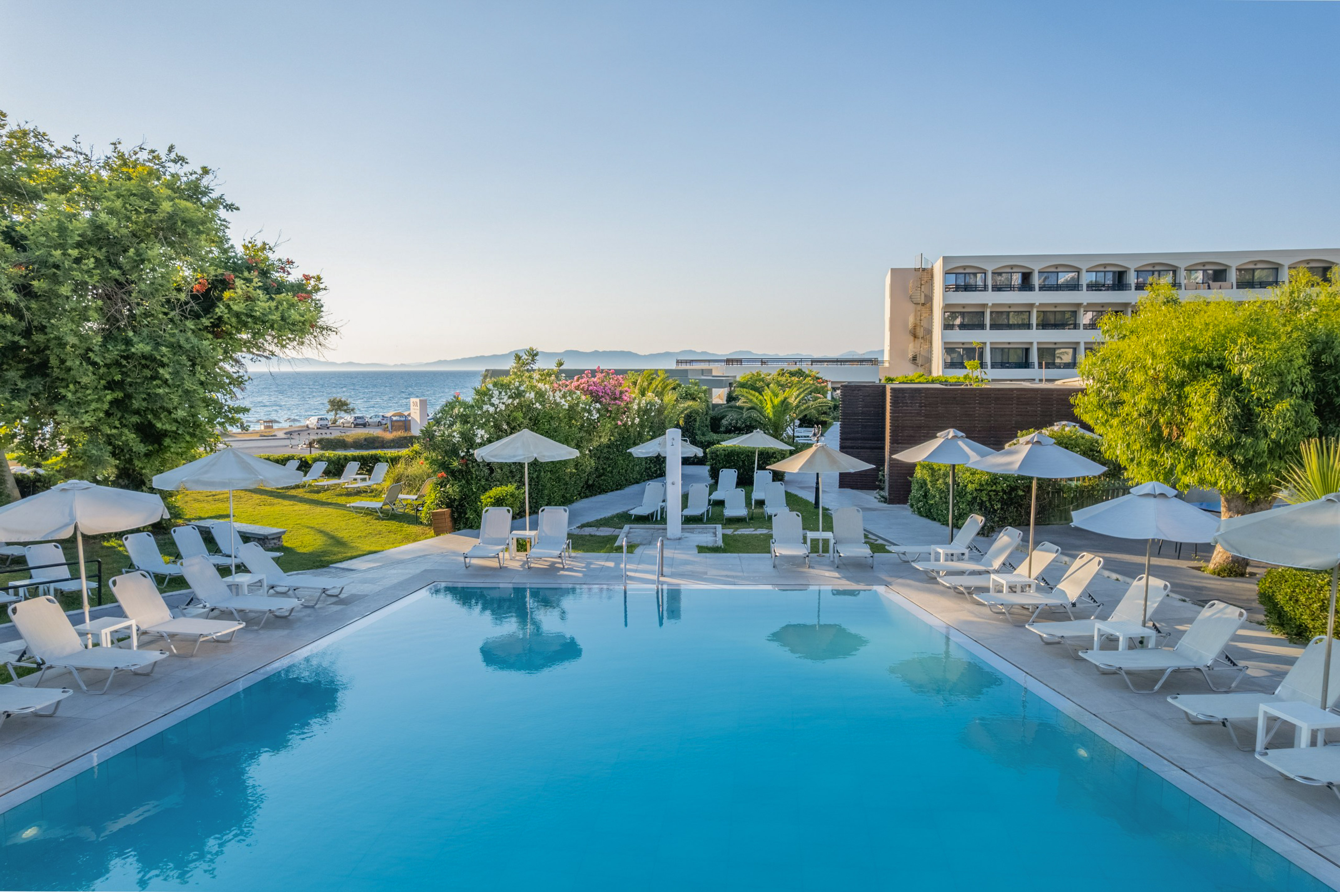 Resort hotel pool, sun loungers, umbrellas, ocean view, and lush gardens.