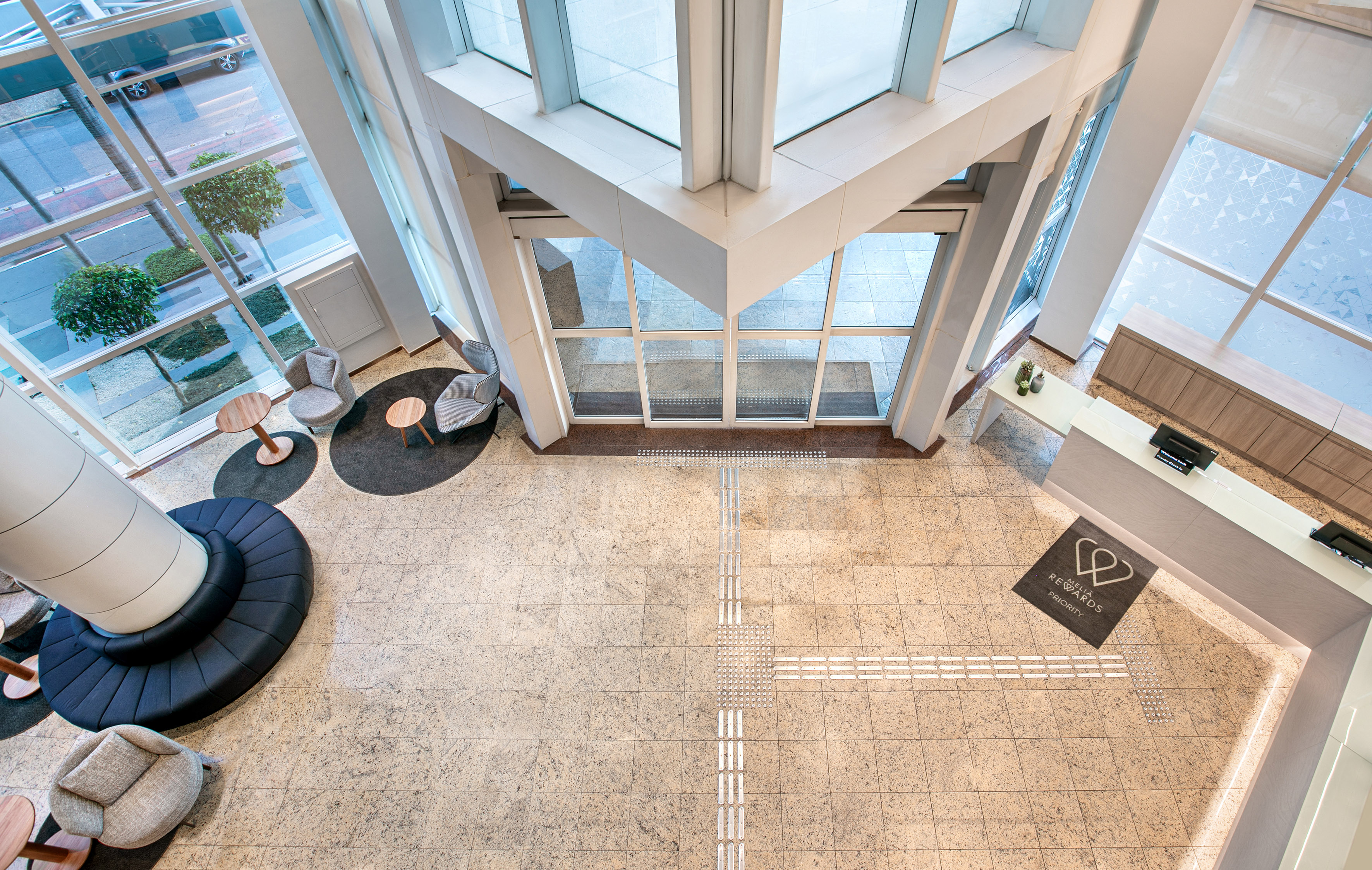 Modern hotel lobby with glass walls, reception desk, and lounge seating.