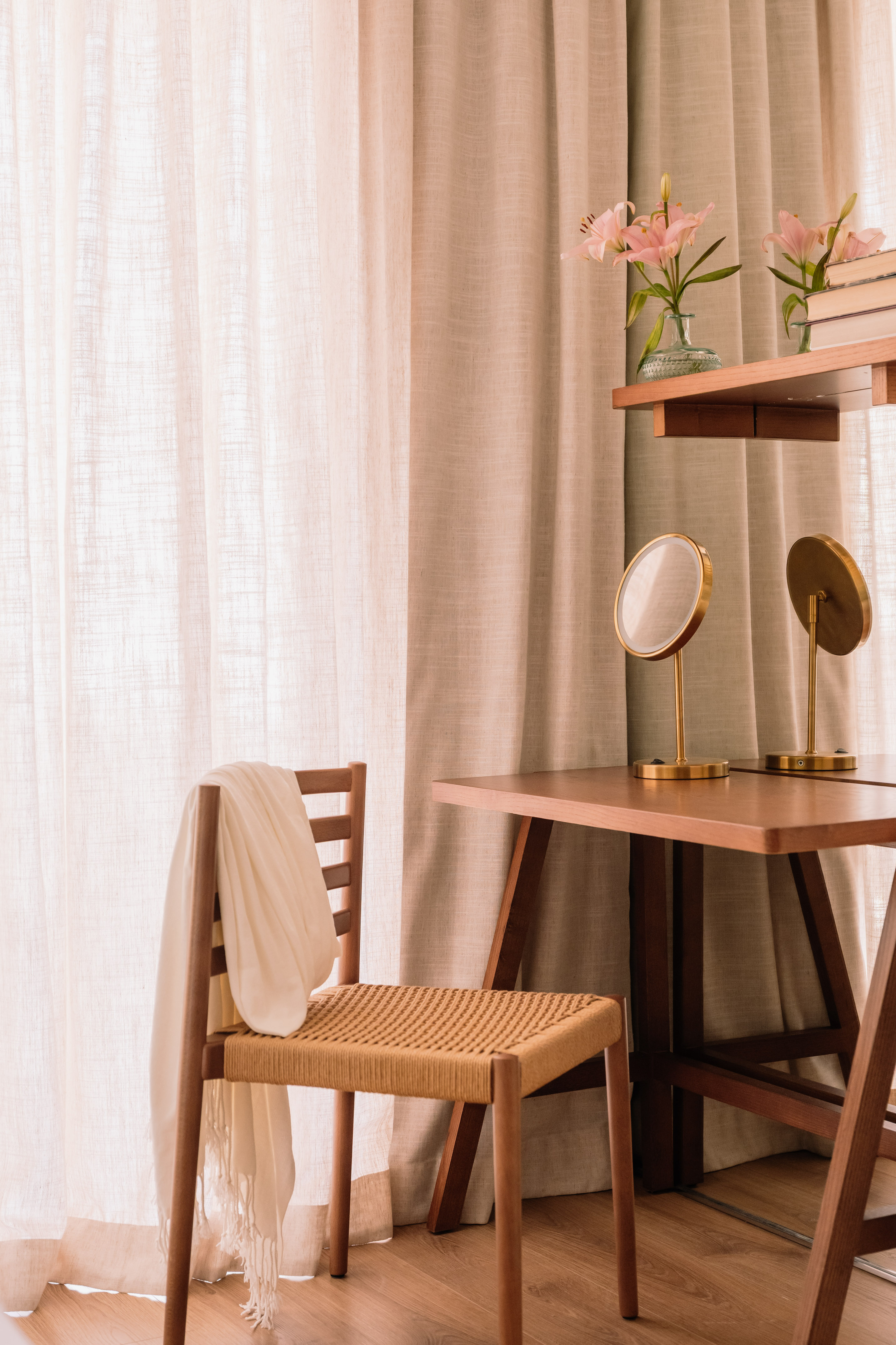 Wooden vanity desk, woven chair, gold mirrors, pink lilies, sheer curtains.