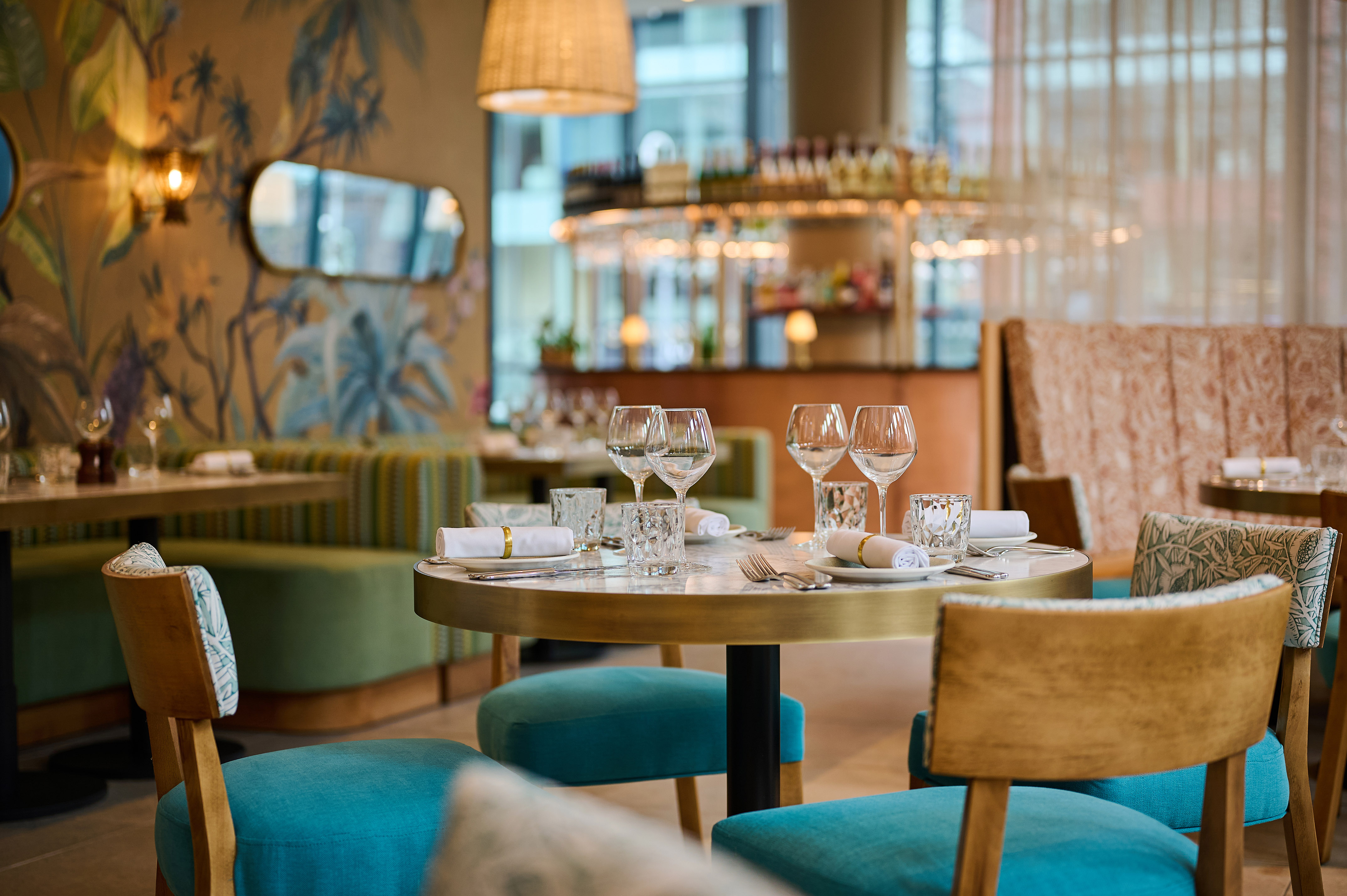 Set dining table in restaurant with blue chairs and tropical wallpaper.