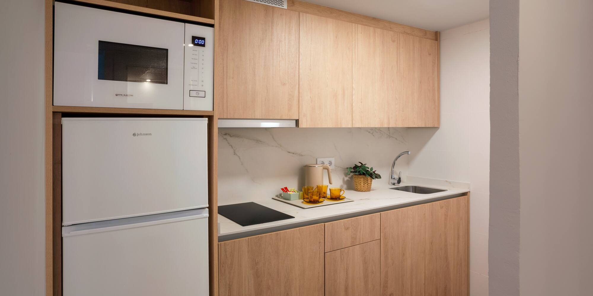 Modern kitchenette with light wood cabinets, white appliances, and marble backsplash.