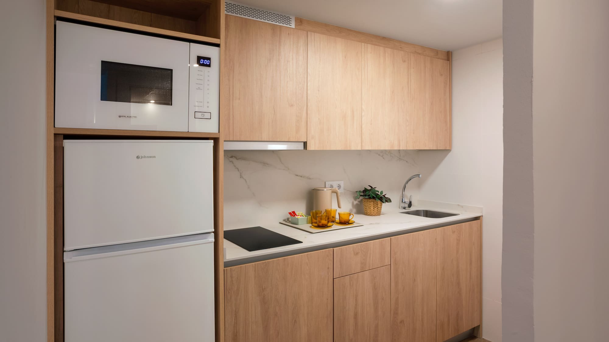 Modern kitchenette with light wood cabinets, white appliances, and marble backsplash.