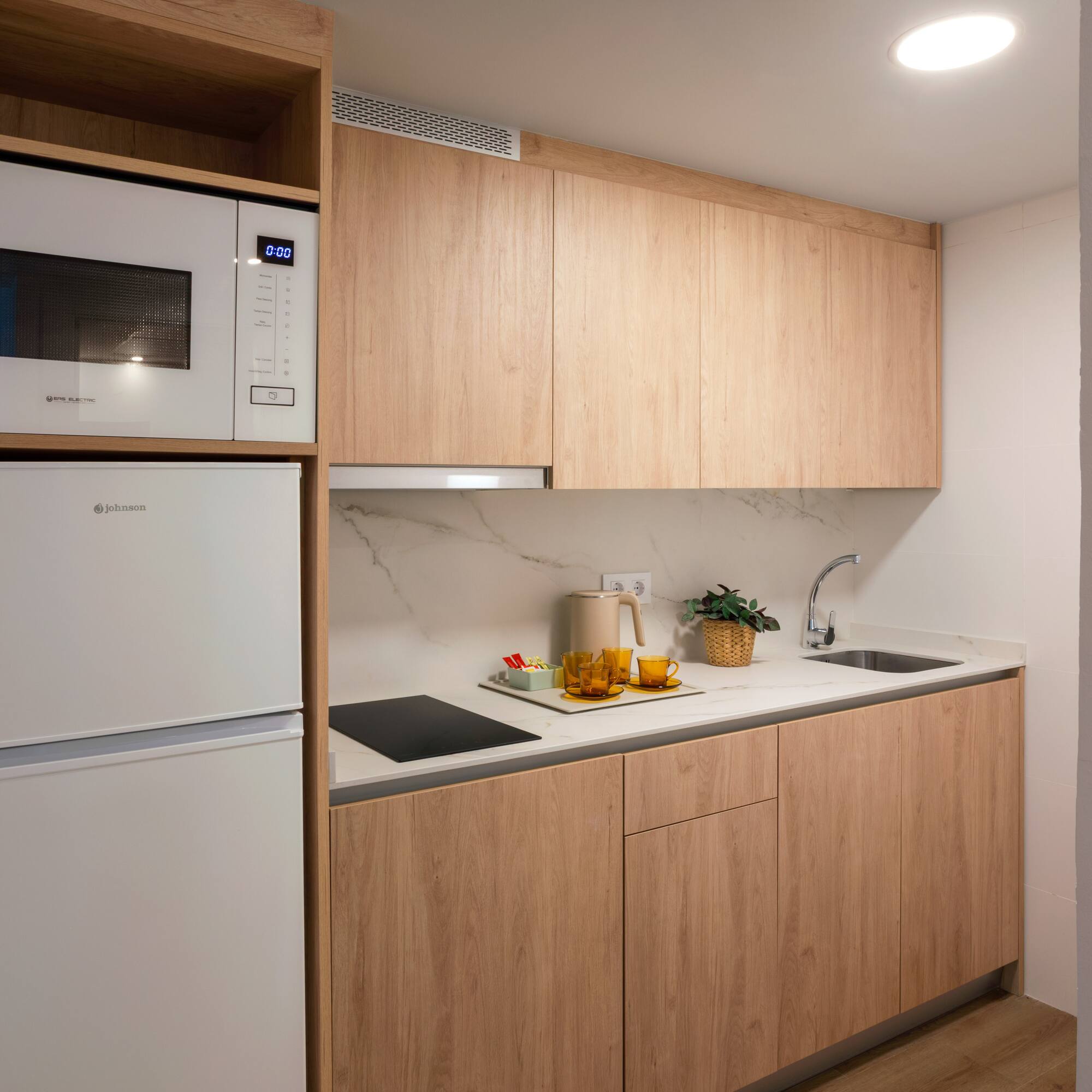 Modern kitchenette with light wood cabinets, white appliances, and marble backsplash.