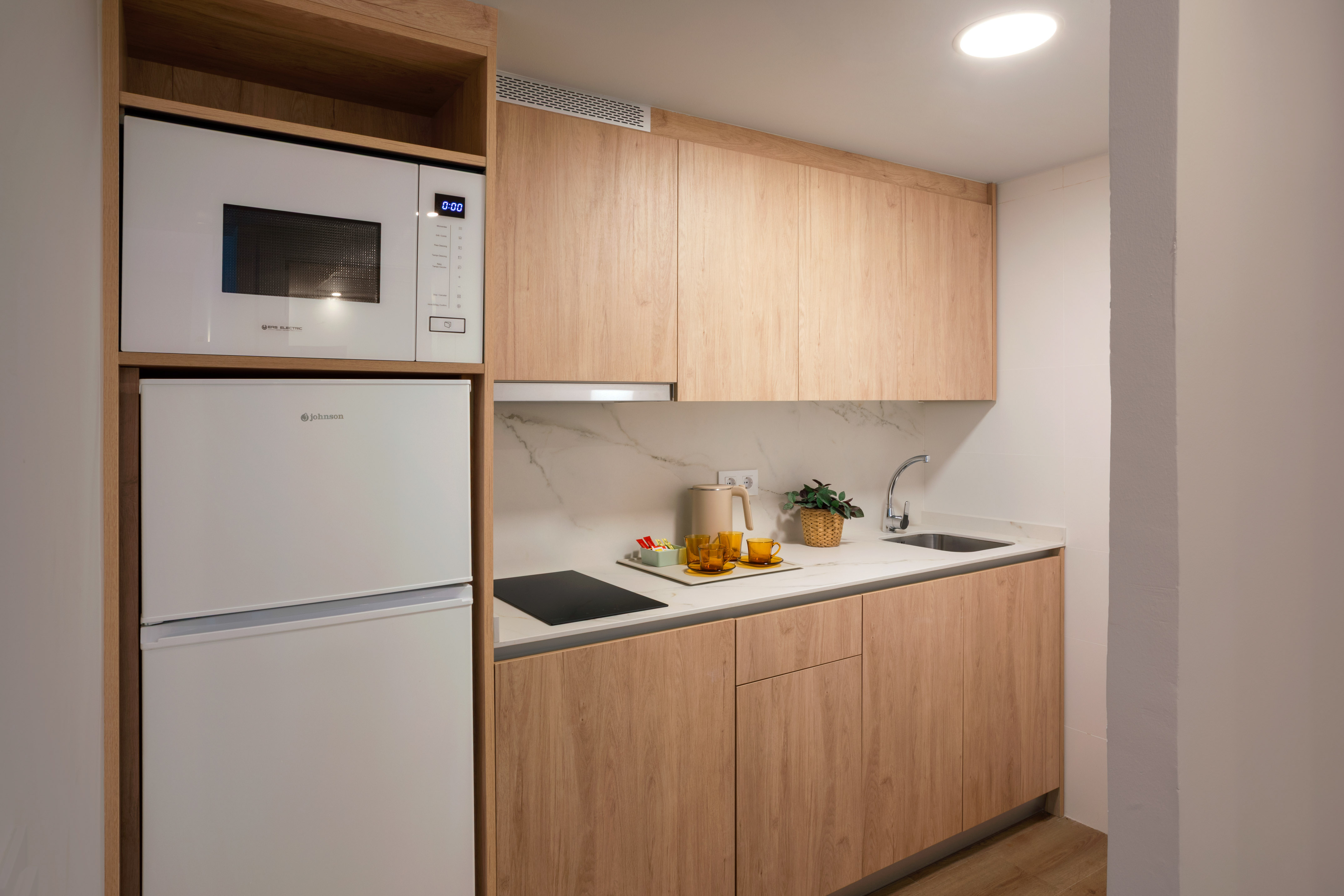 Modern kitchenette with wood cabinets, white appliances, and marble counter.