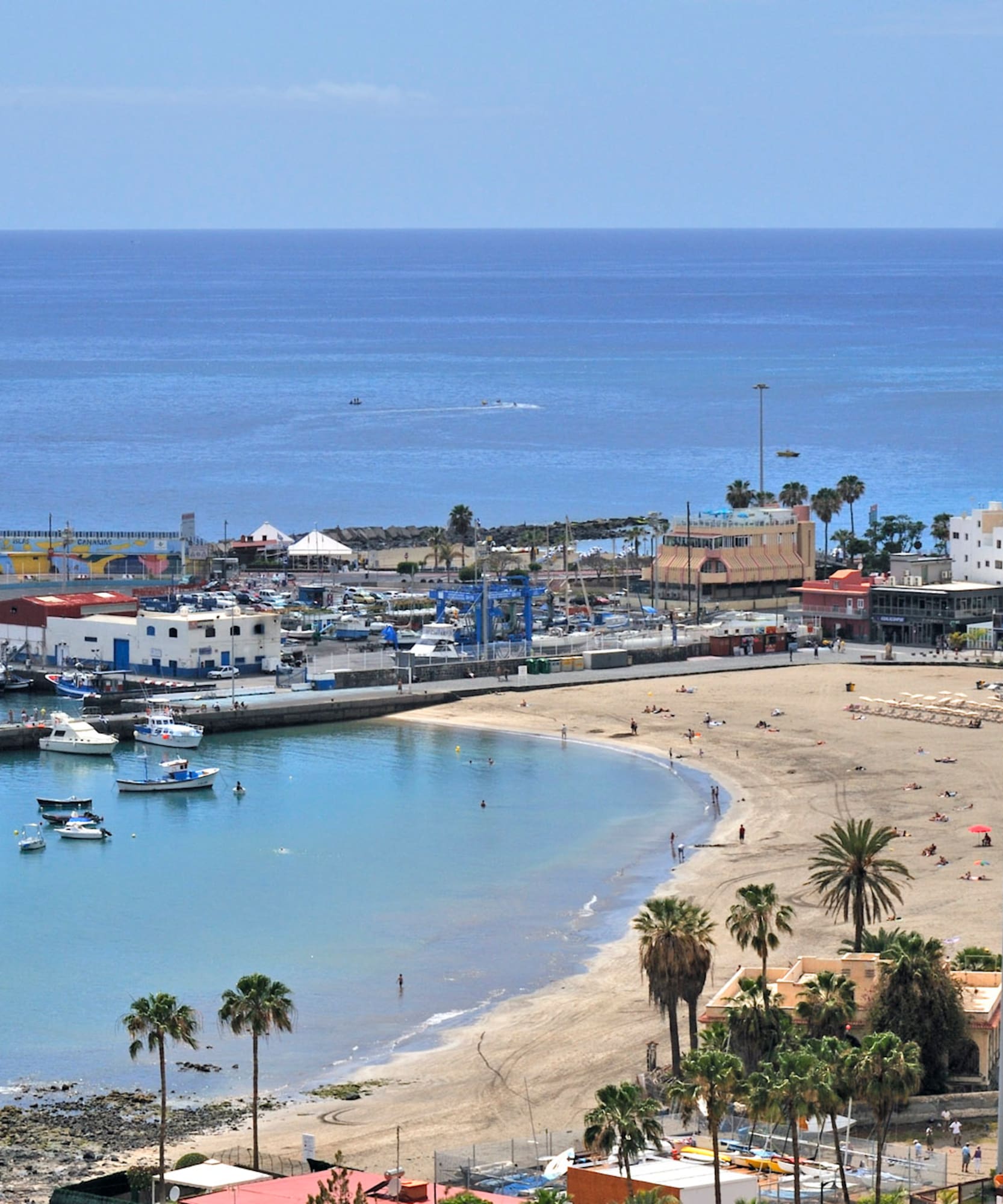 Playa Los Cristianos, Tenerife, con puerto de barcos, arena y palmeras.