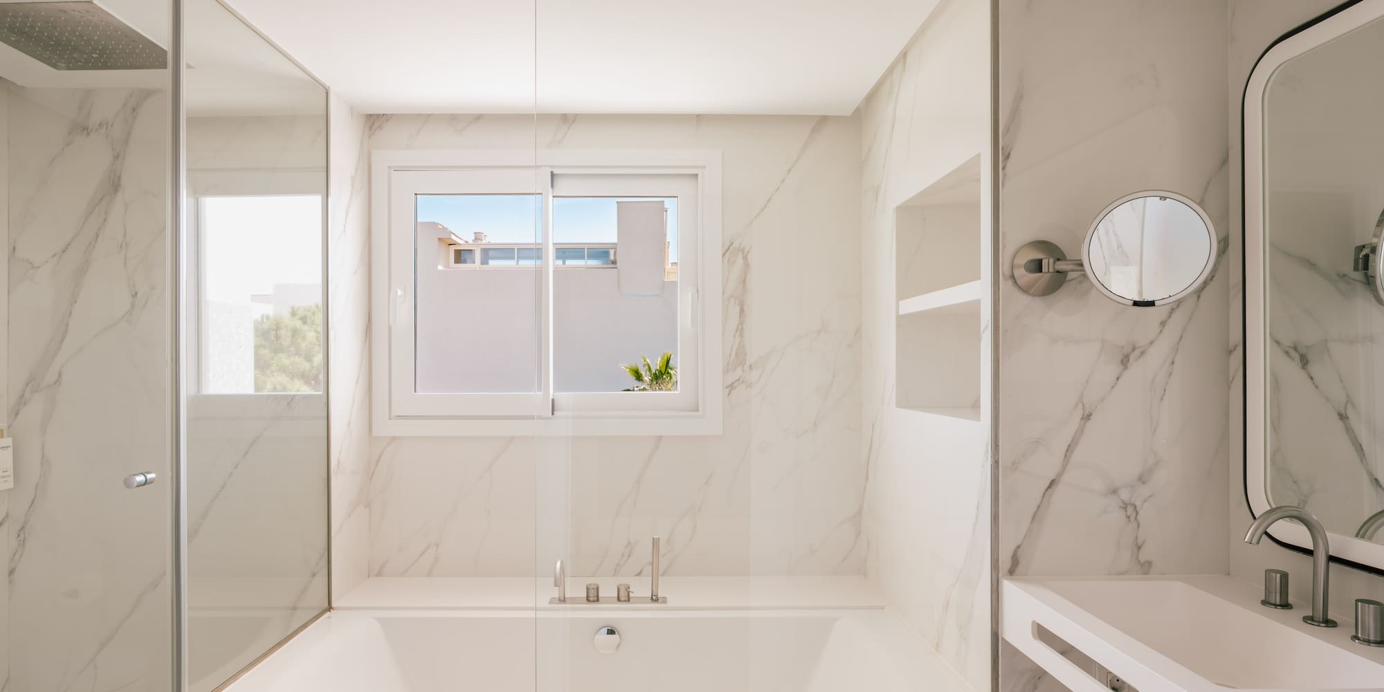 Modern white marble bathroom with bathtub, glass shower, and vanity.