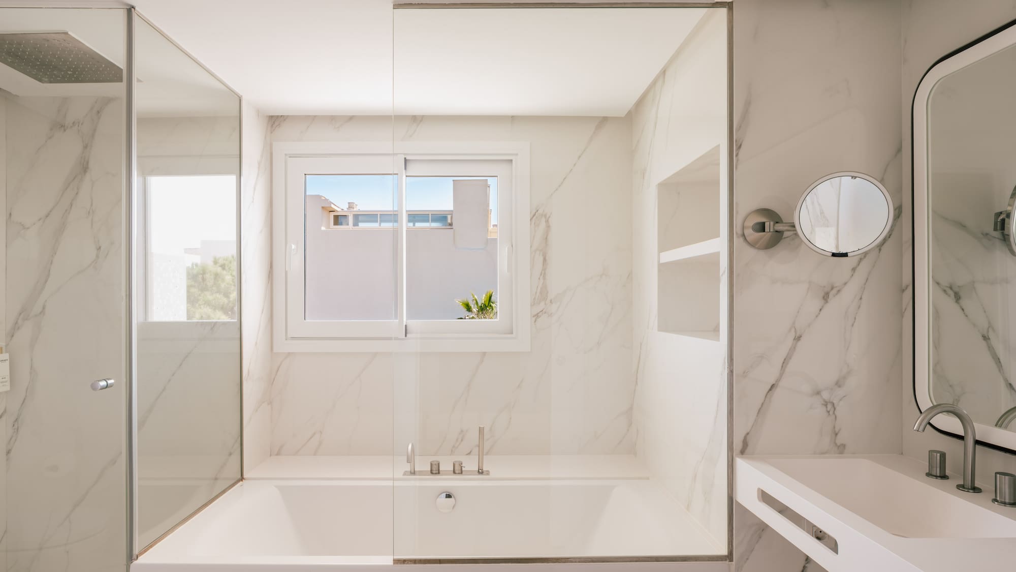 Modern white marble bathroom with bathtub, glass shower, and vanity.
