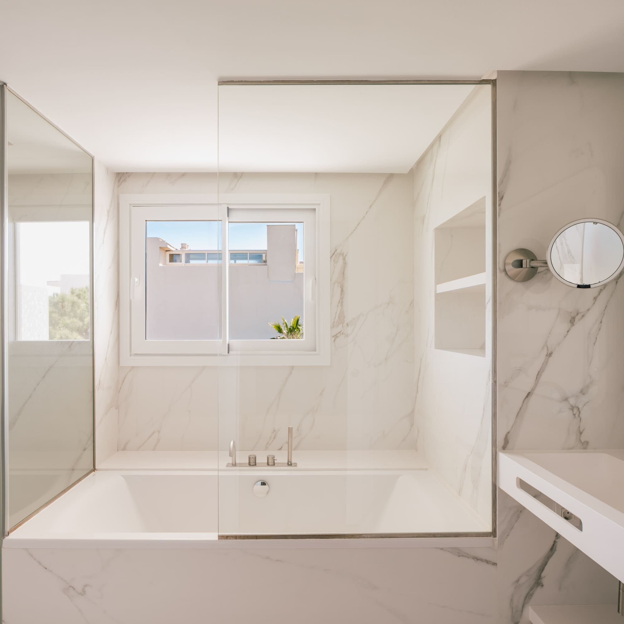 Modern white marble bathroom with bathtub, glass shower, and vanity.