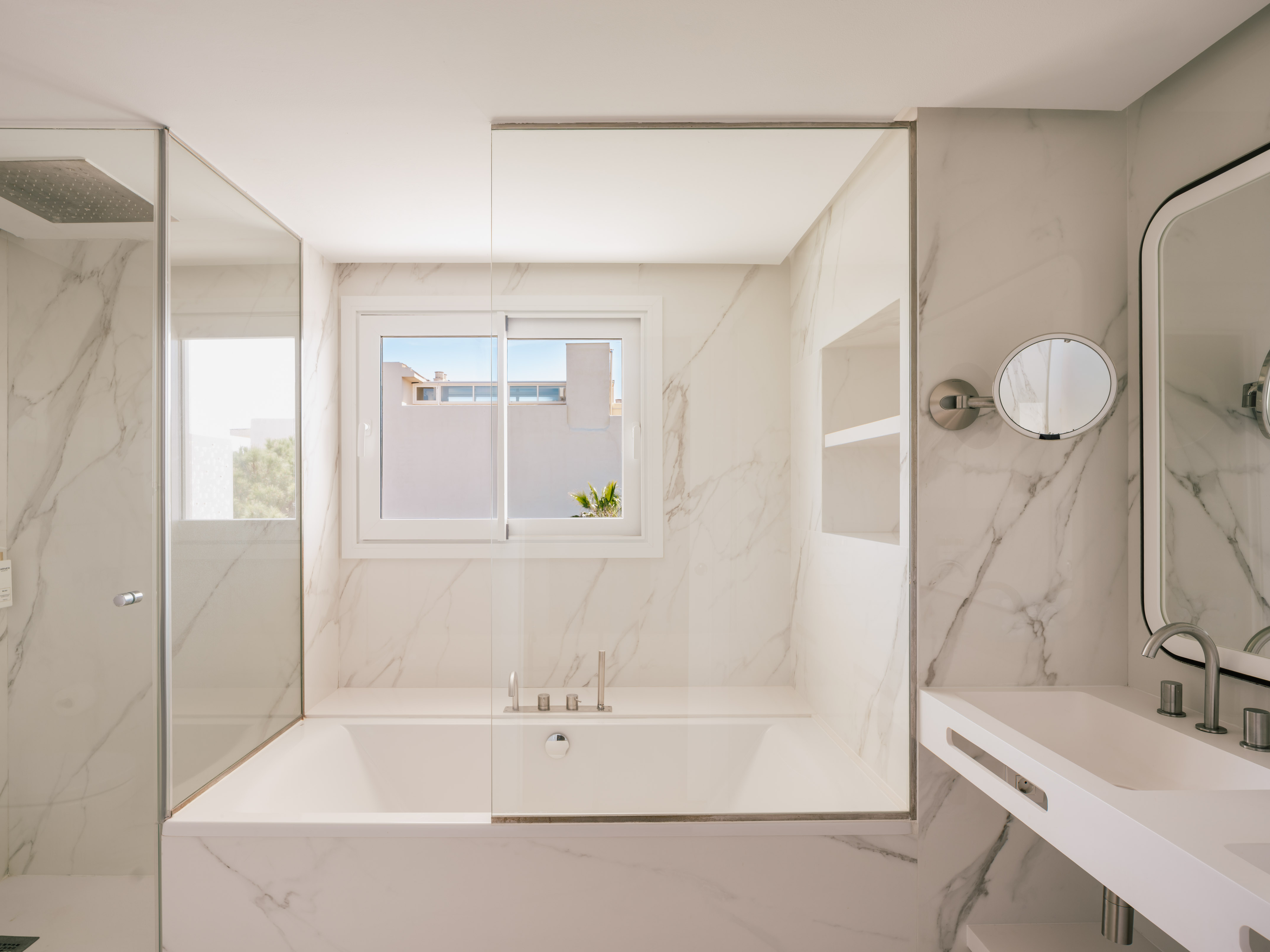 Modern white marble bathroom with bathtub, glass shower, and vanity.
