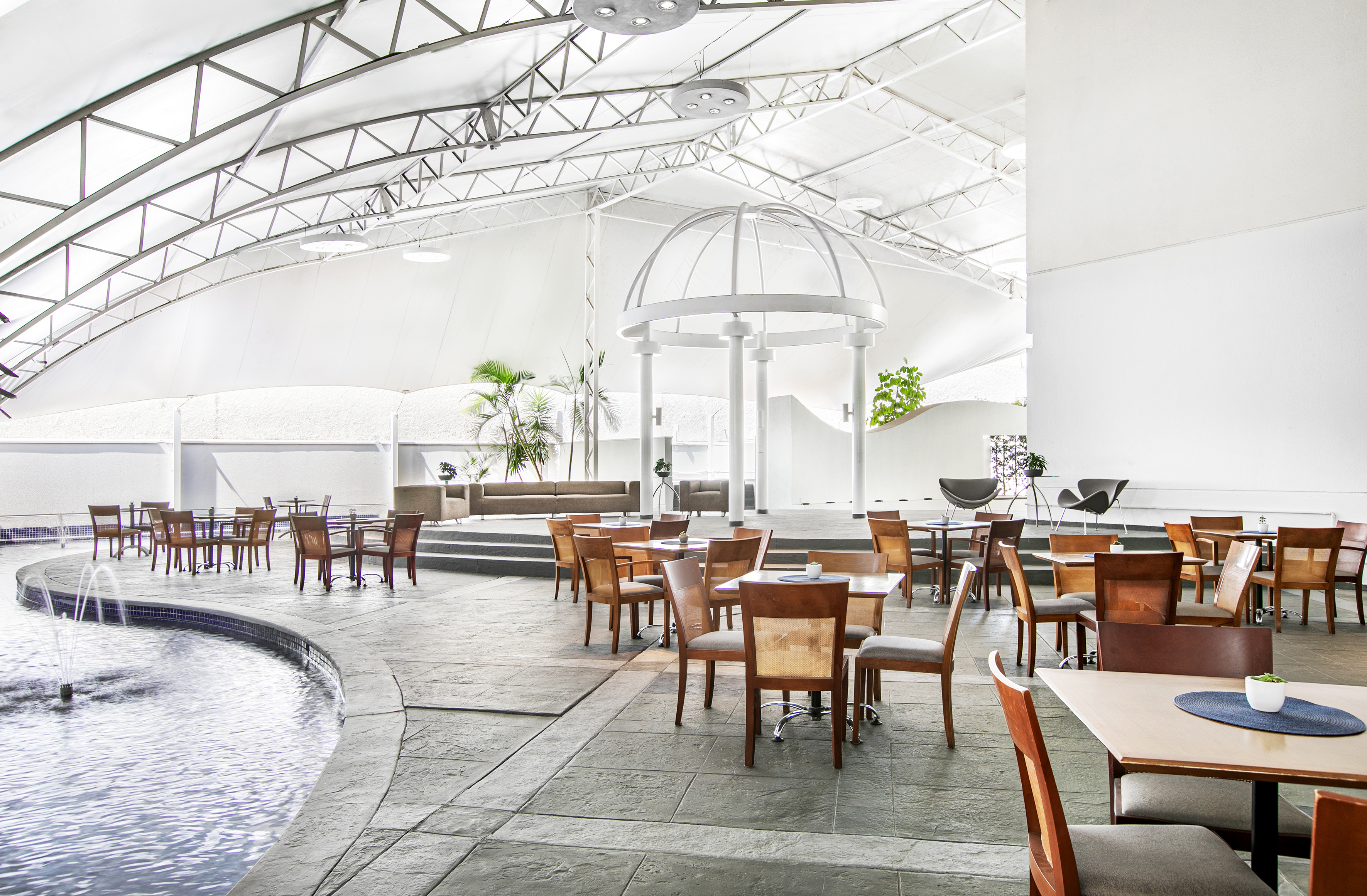 Modern restaurant with indoor fountain, dining tables, and tensile roof.