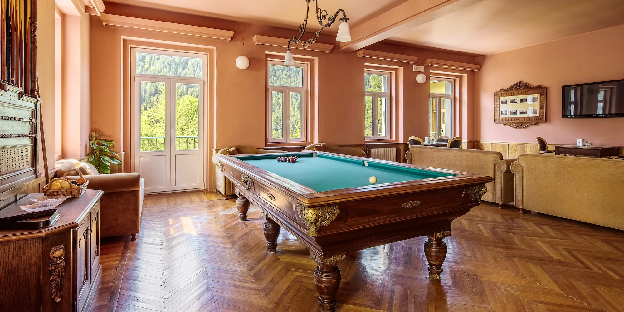 Elegant billiard room with vintage pool table, herringbone floor, and forest view.