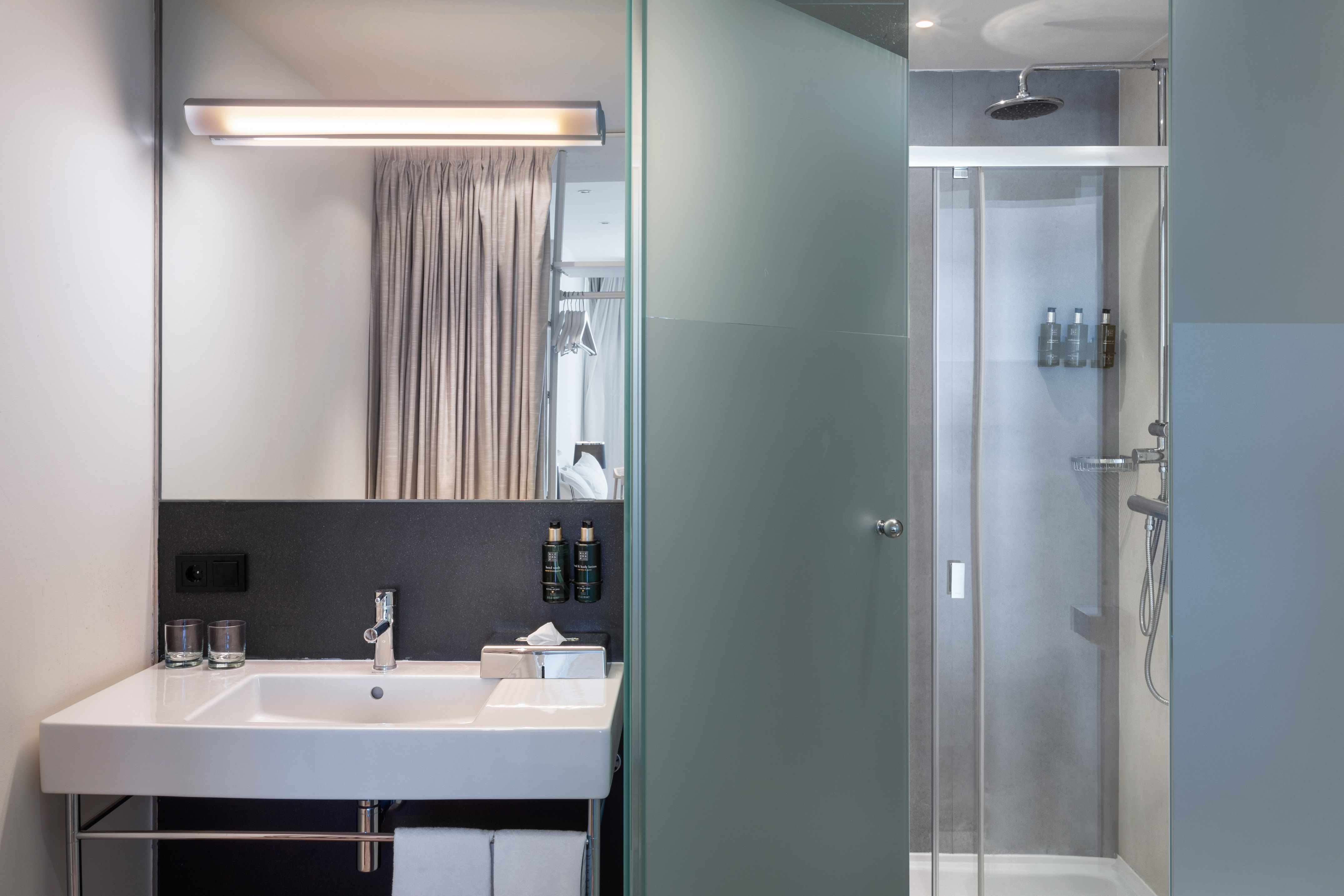 Modern hotel bathroom with white vanity, backlit mirror, and glass shower.