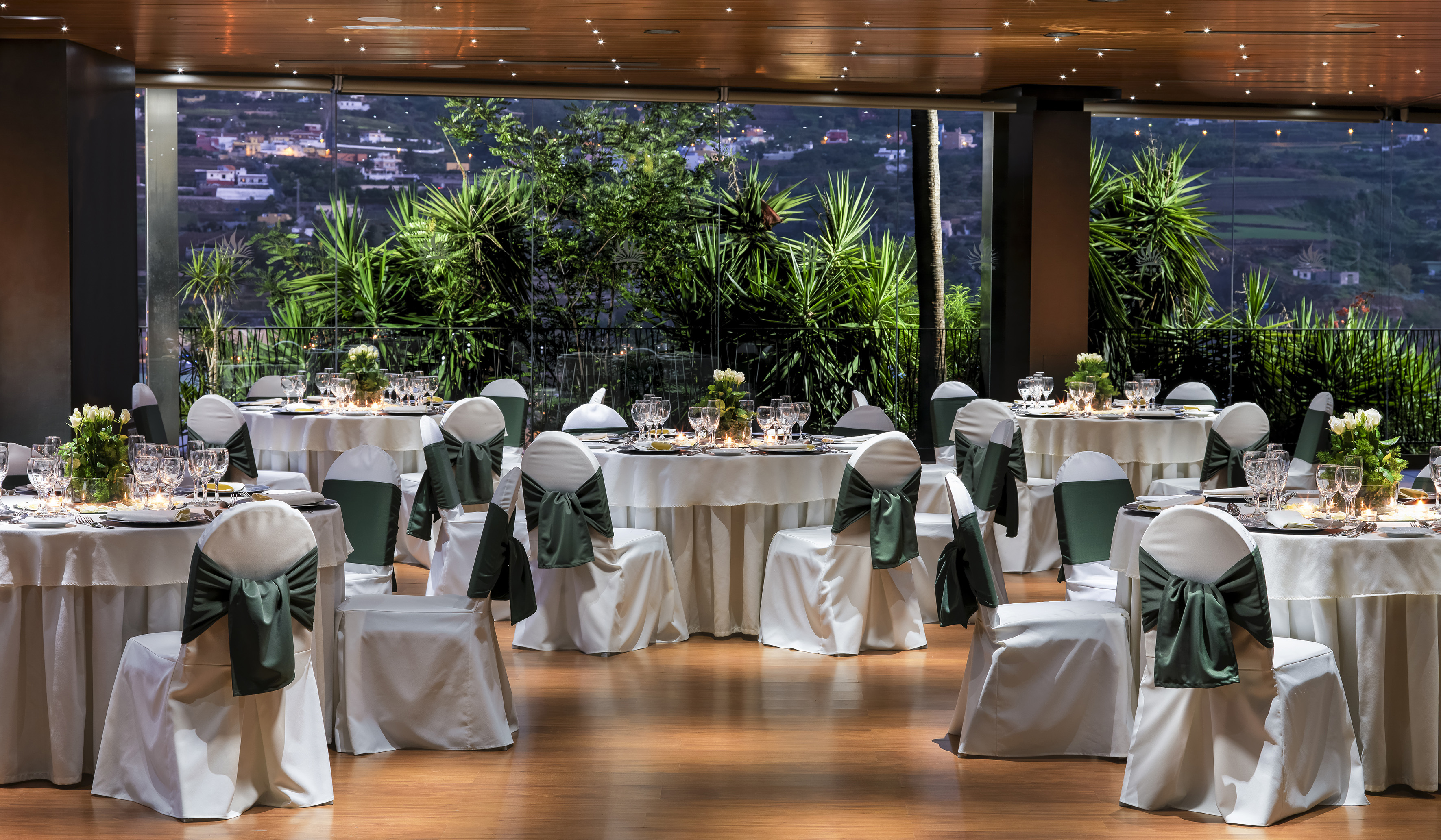 Elegant dining hall with green sashed chairs and evening landscape view.