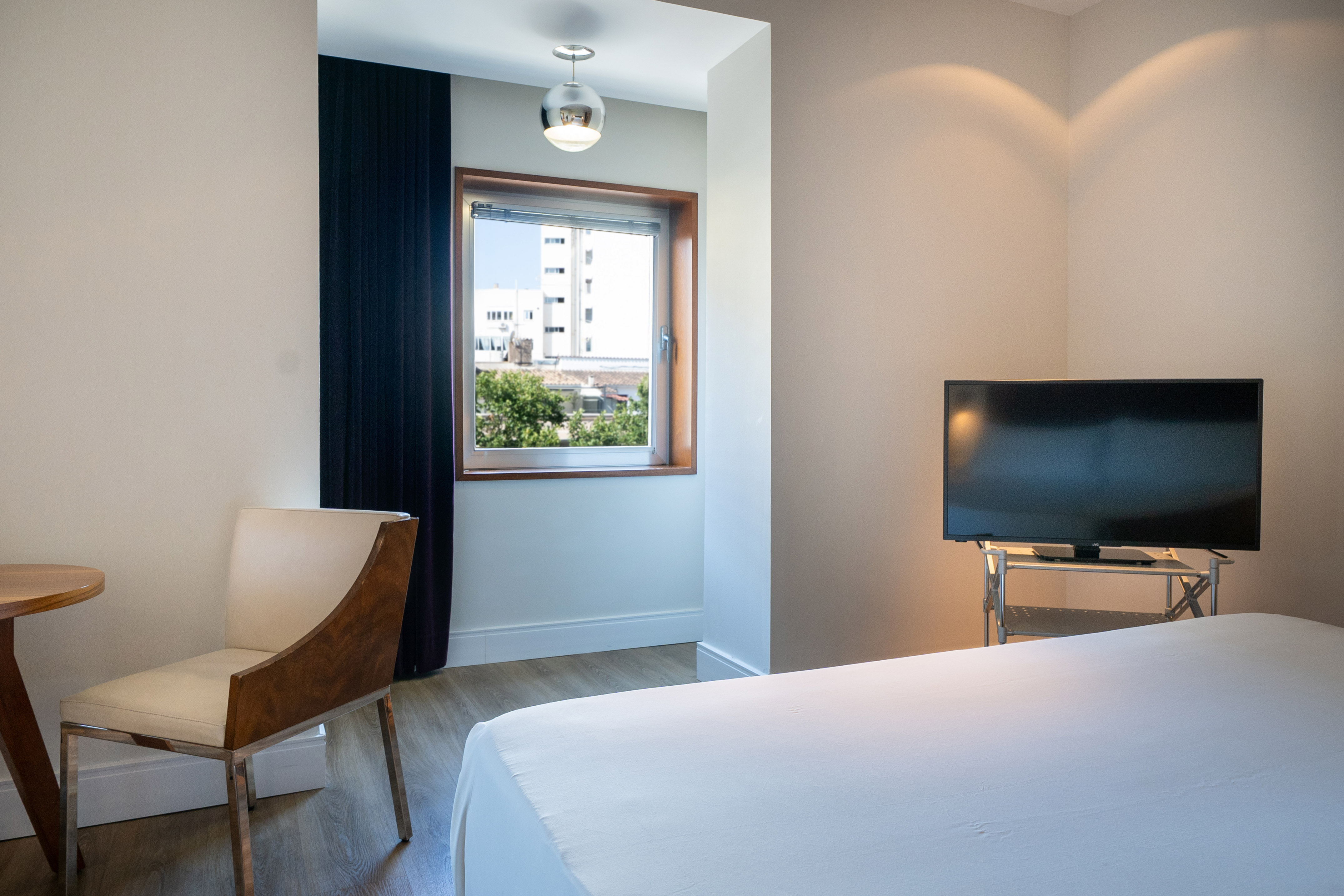Modern hotel room with bed, flat-screen TV, contemporary chair, and city view.