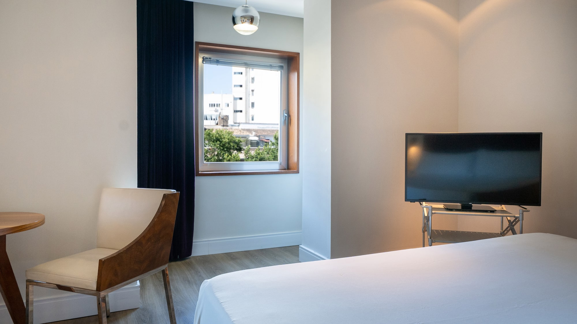 Modern hotel room with bed, flat-screen TV, contemporary chair, and city view.