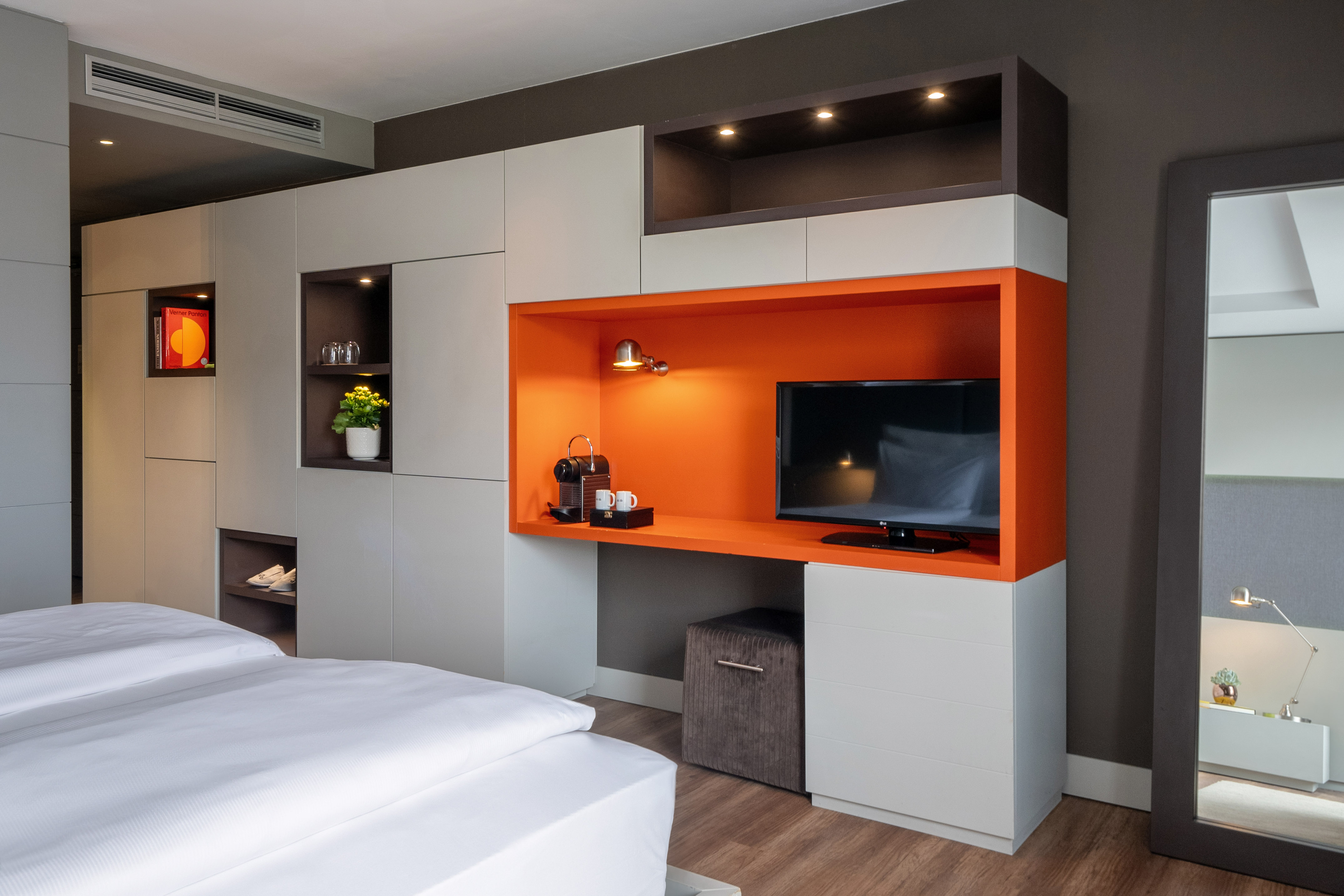 Modern hotel room with orange TV unit, coffee maker, and integrated storage.