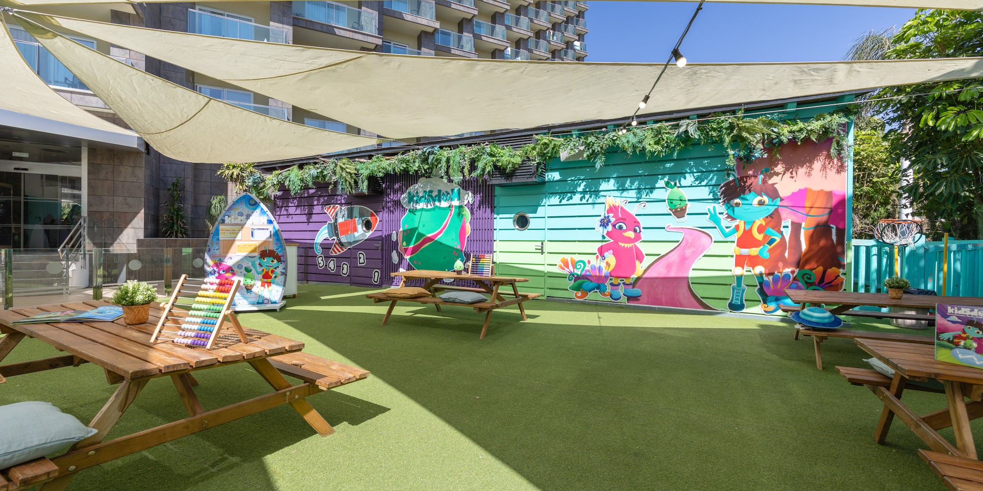 Hotel outdoor kids' club with vibrant murals, artificial turf, and picnic tables.