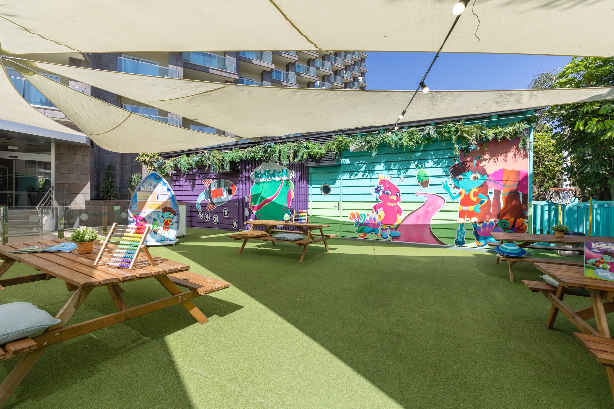 Hotel outdoor kids' club with vibrant murals, artificial turf, and picnic tables.