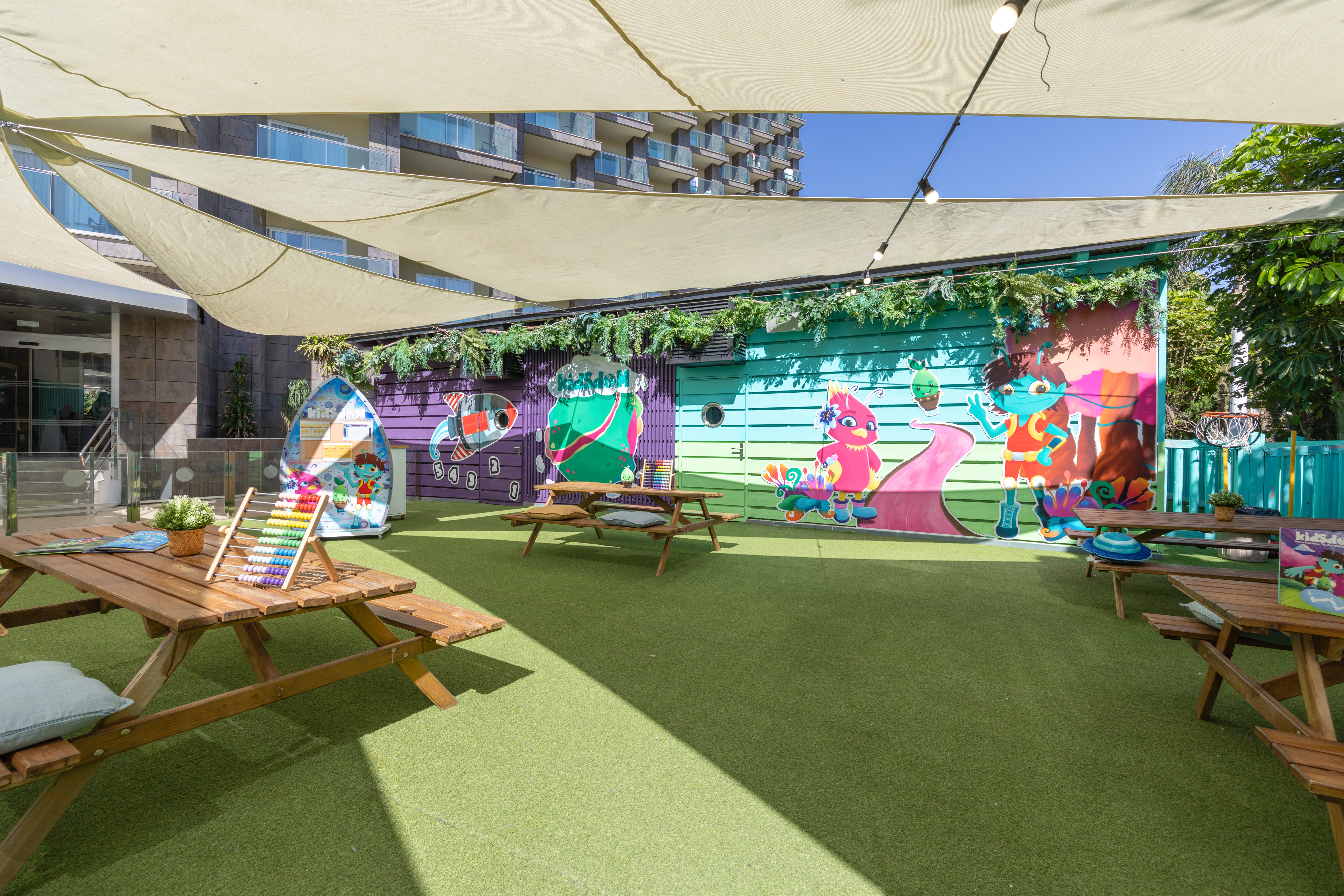 Hotel outdoor kids' club with vibrant murals, artificial turf, and picnic tables.