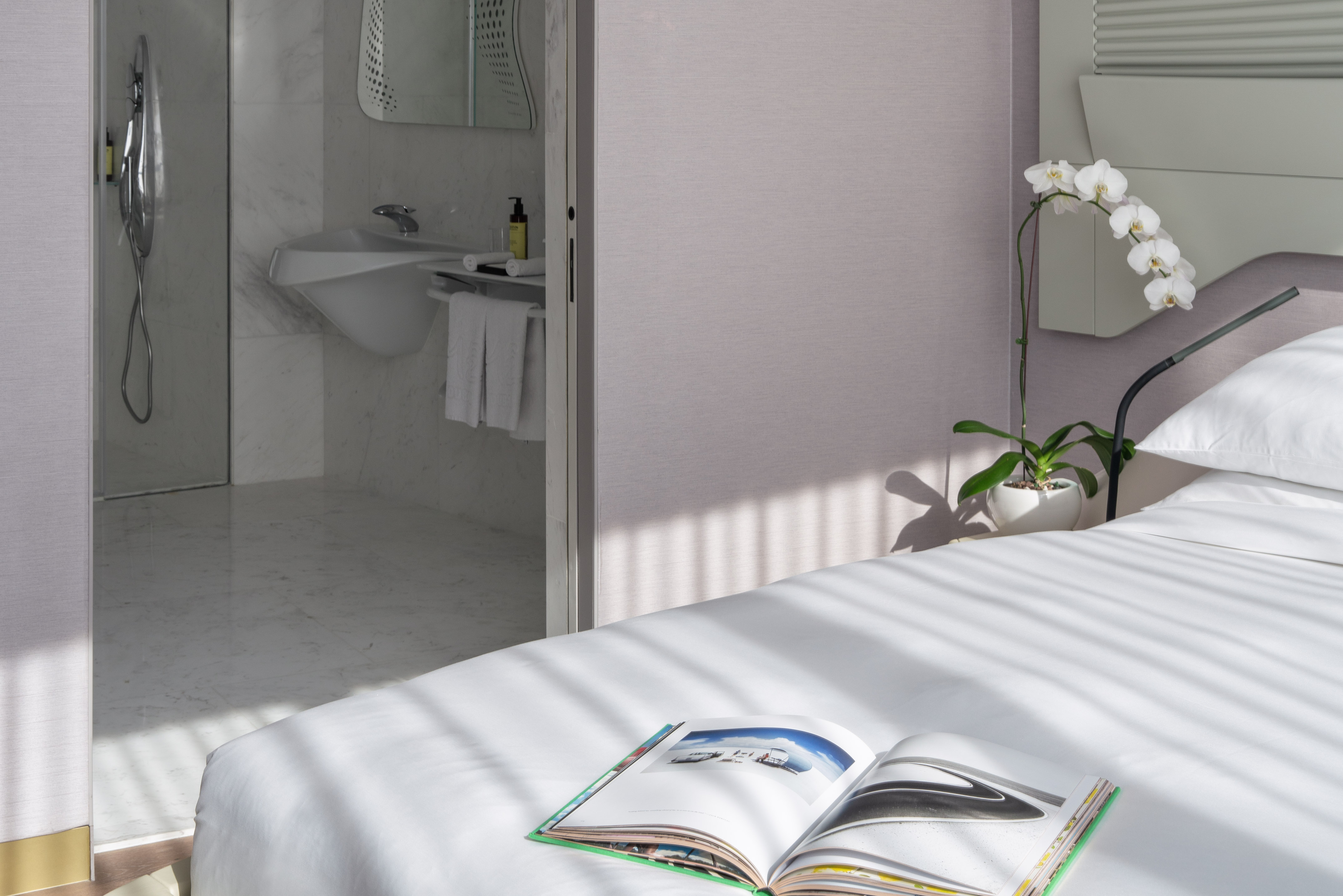 Bright hotel bedroom with white bed, open book, orchid, and marble bathroom. - 1 Bedroom ME Signature Residence - ME Dubai Residences, دبي