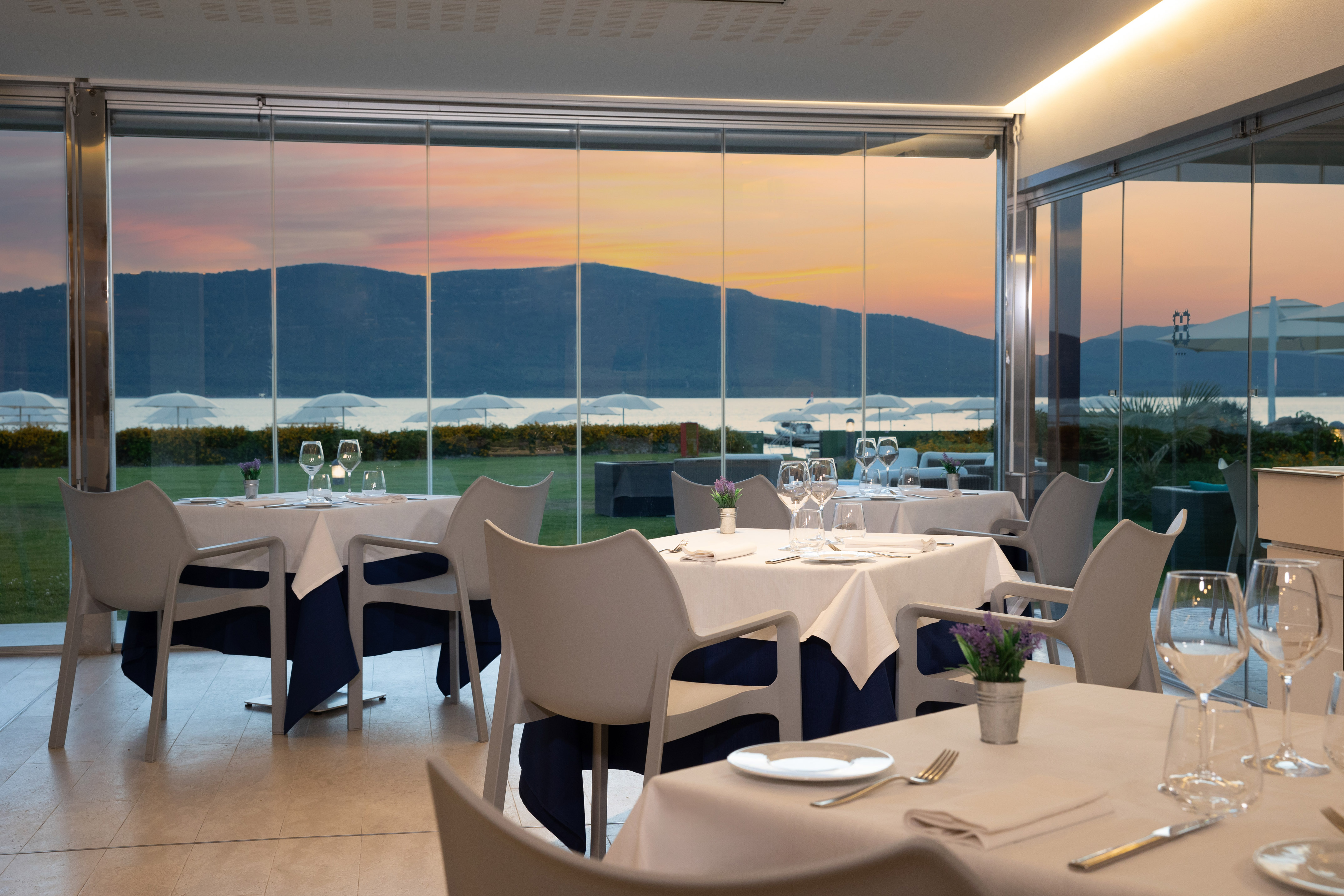 Waterfront restaurant with set tables, large glass windows, and sunset lake view.