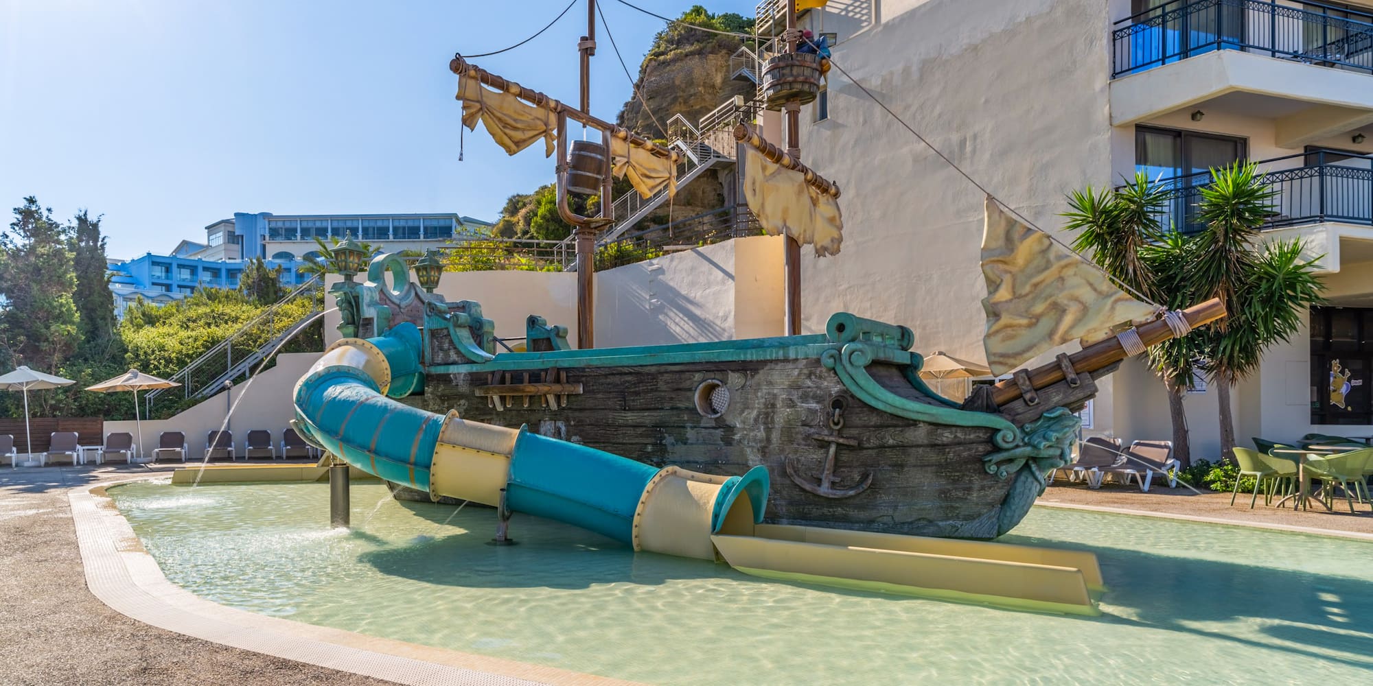 Children's pirate ship water slide at a sunny hotel pool.