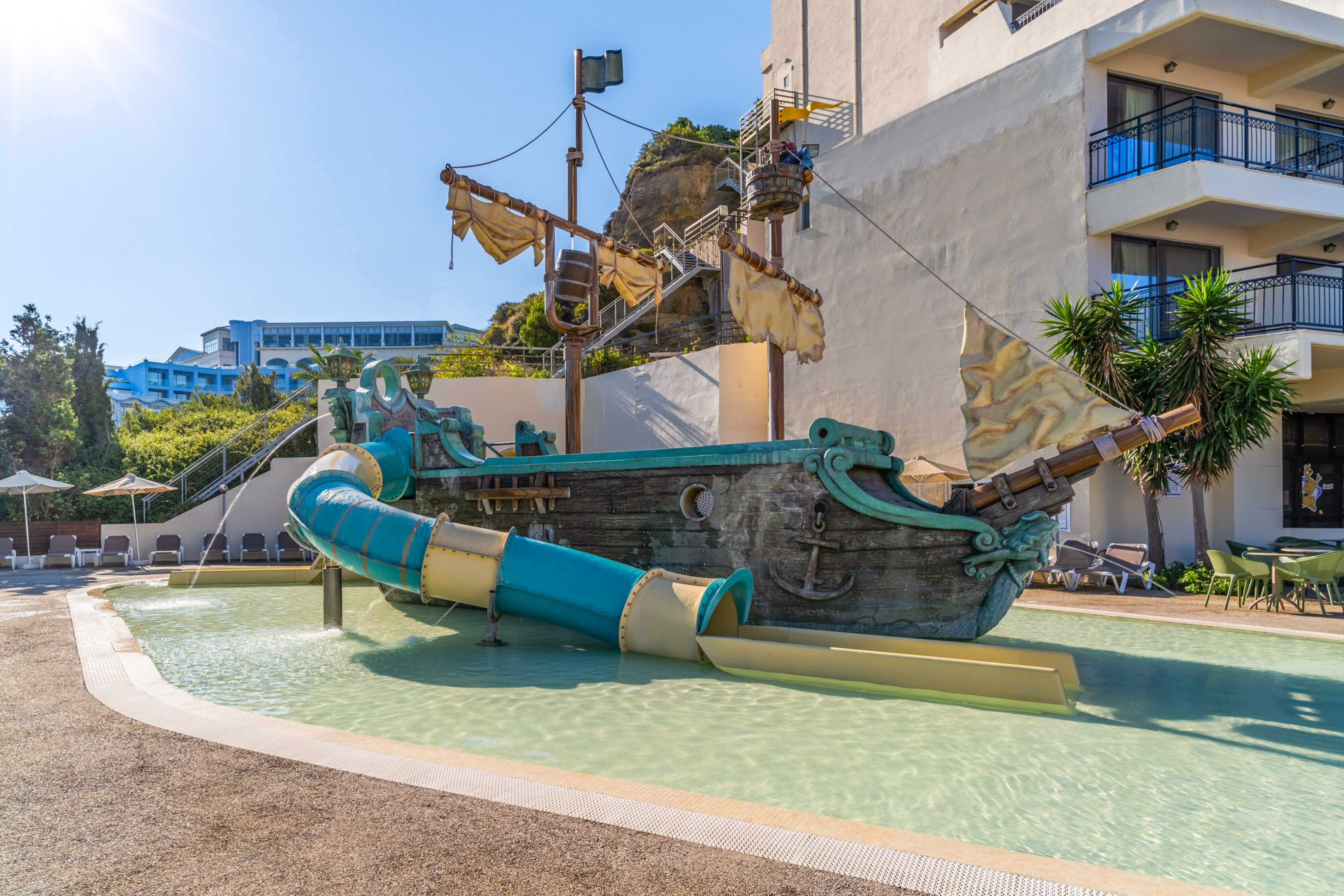 Children's pirate ship water slide at a sunny hotel pool.