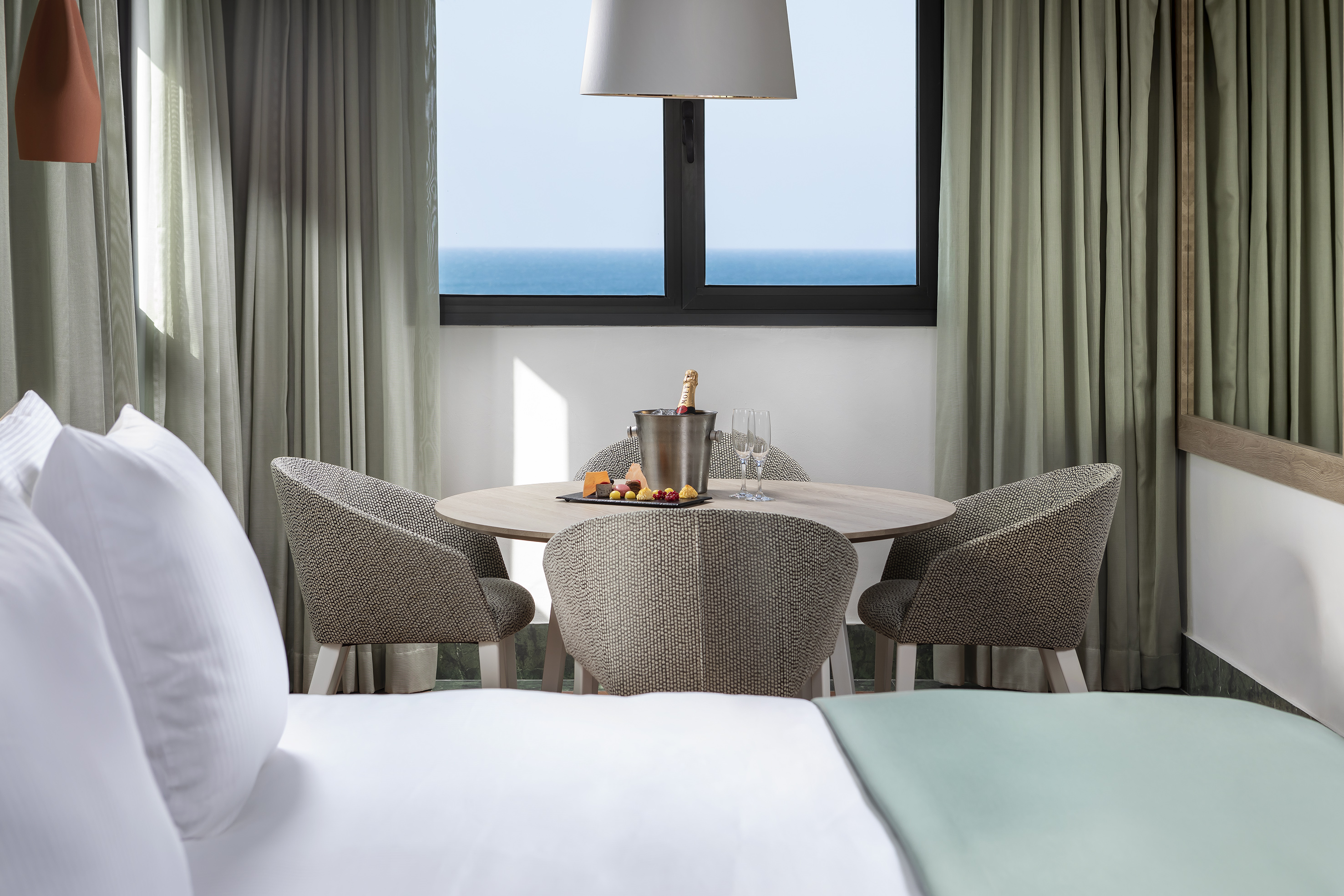 Luxury hotel room with ocean view, dining area, champagne, and bed.
