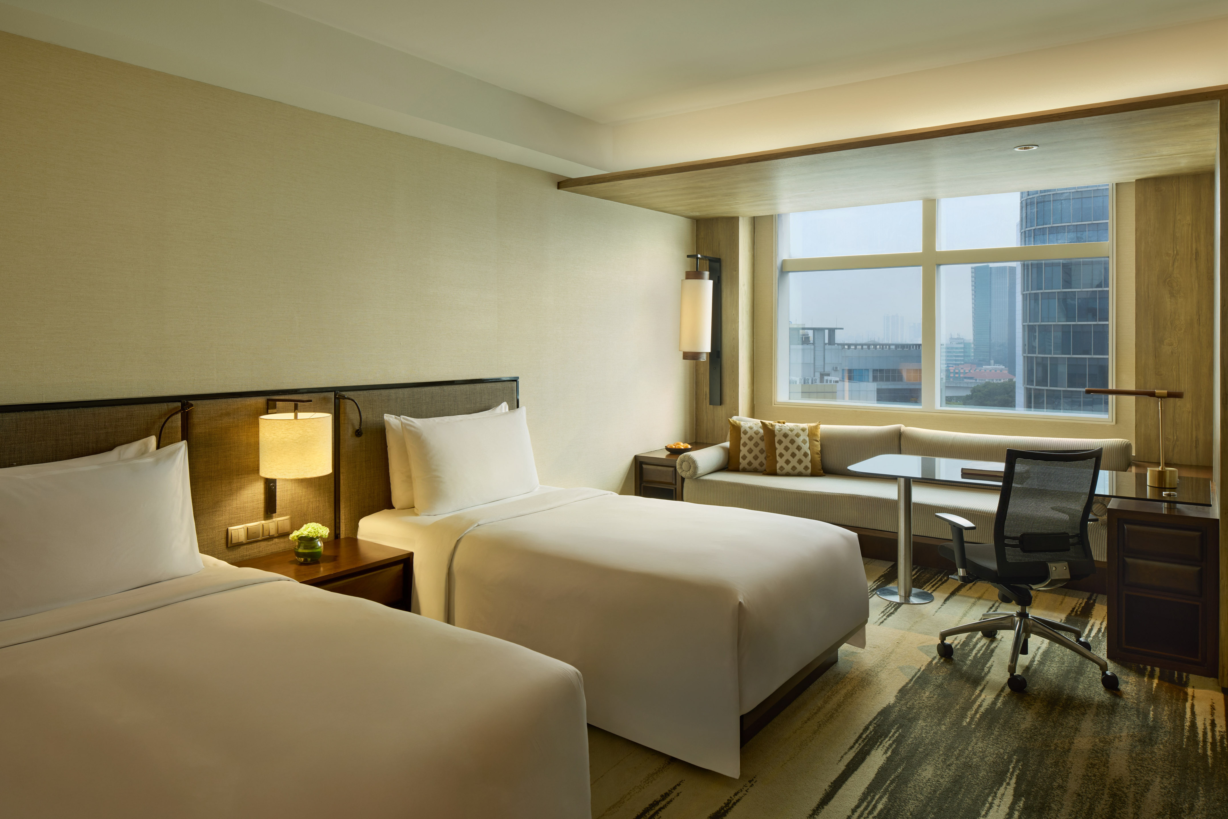 Hotel room with two twin beds, city view, desk, and window seating area.