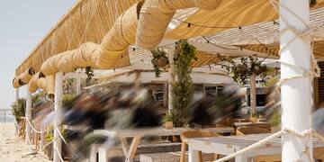 a beach covered area with a wooden deck and tables and chairs