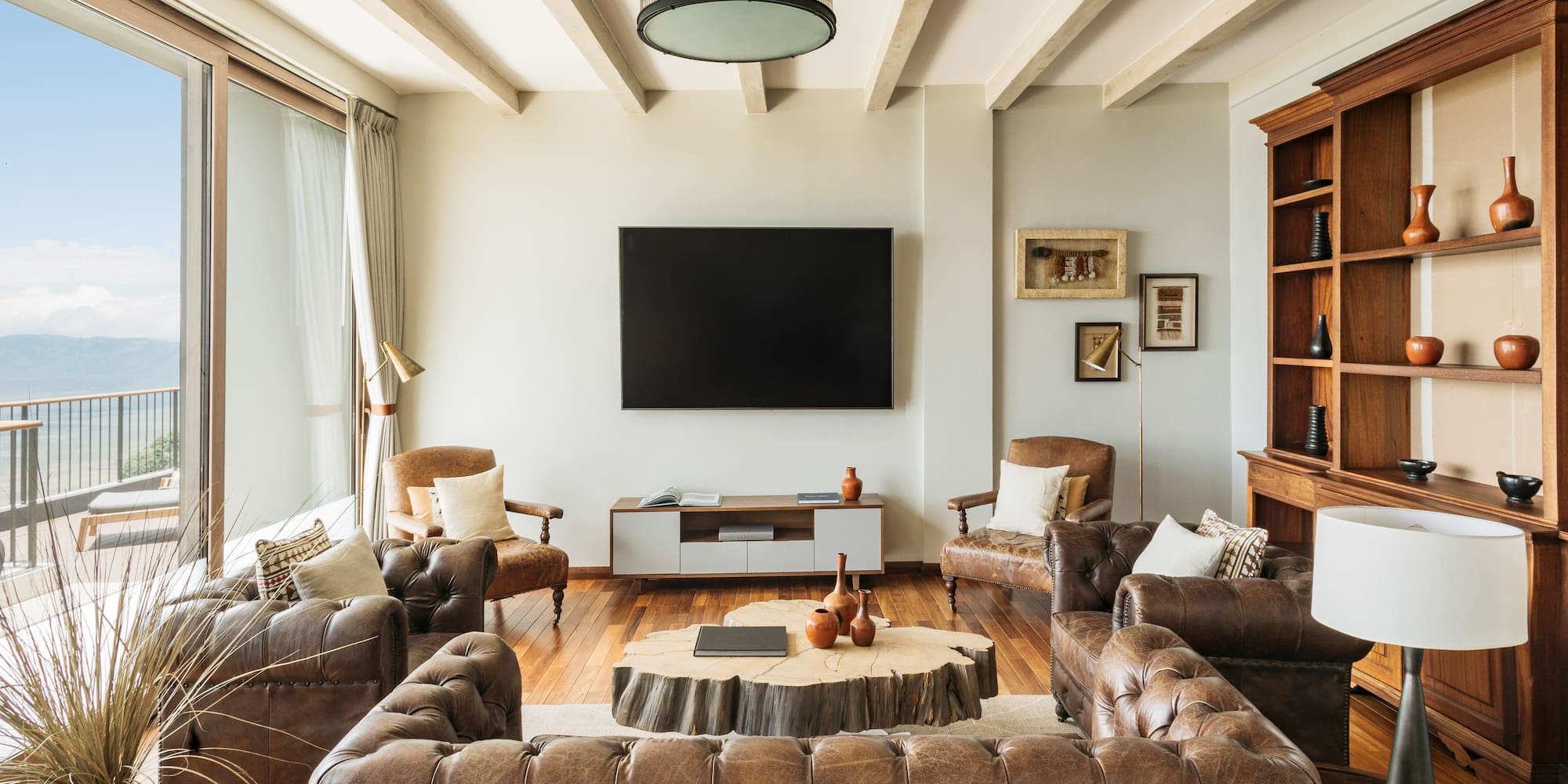 Rustic modern living room, brown leather sofas, wood coffee table, balcony view.