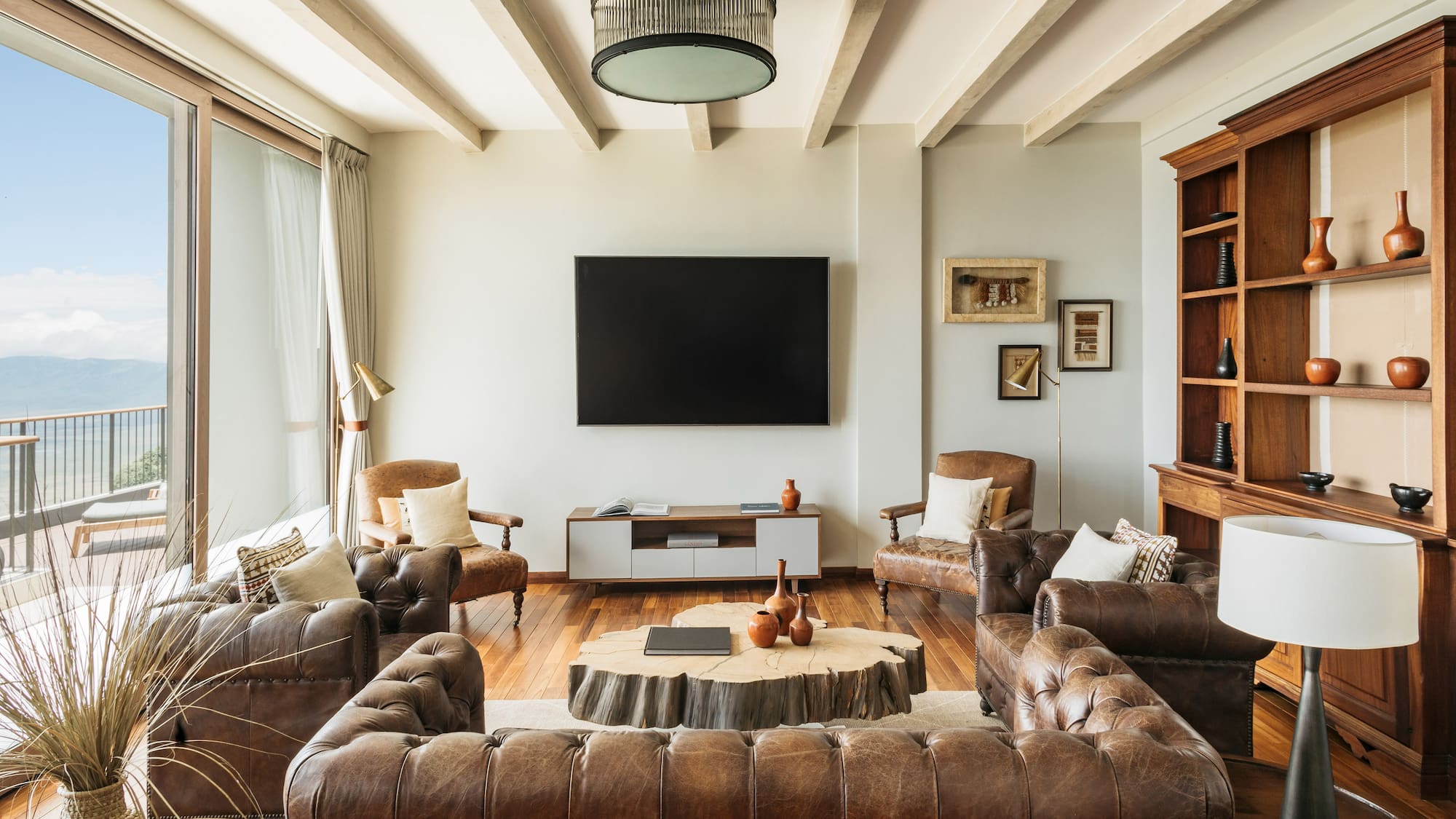 Rustic modern living room, brown leather sofas, wood coffee table, balcony view.