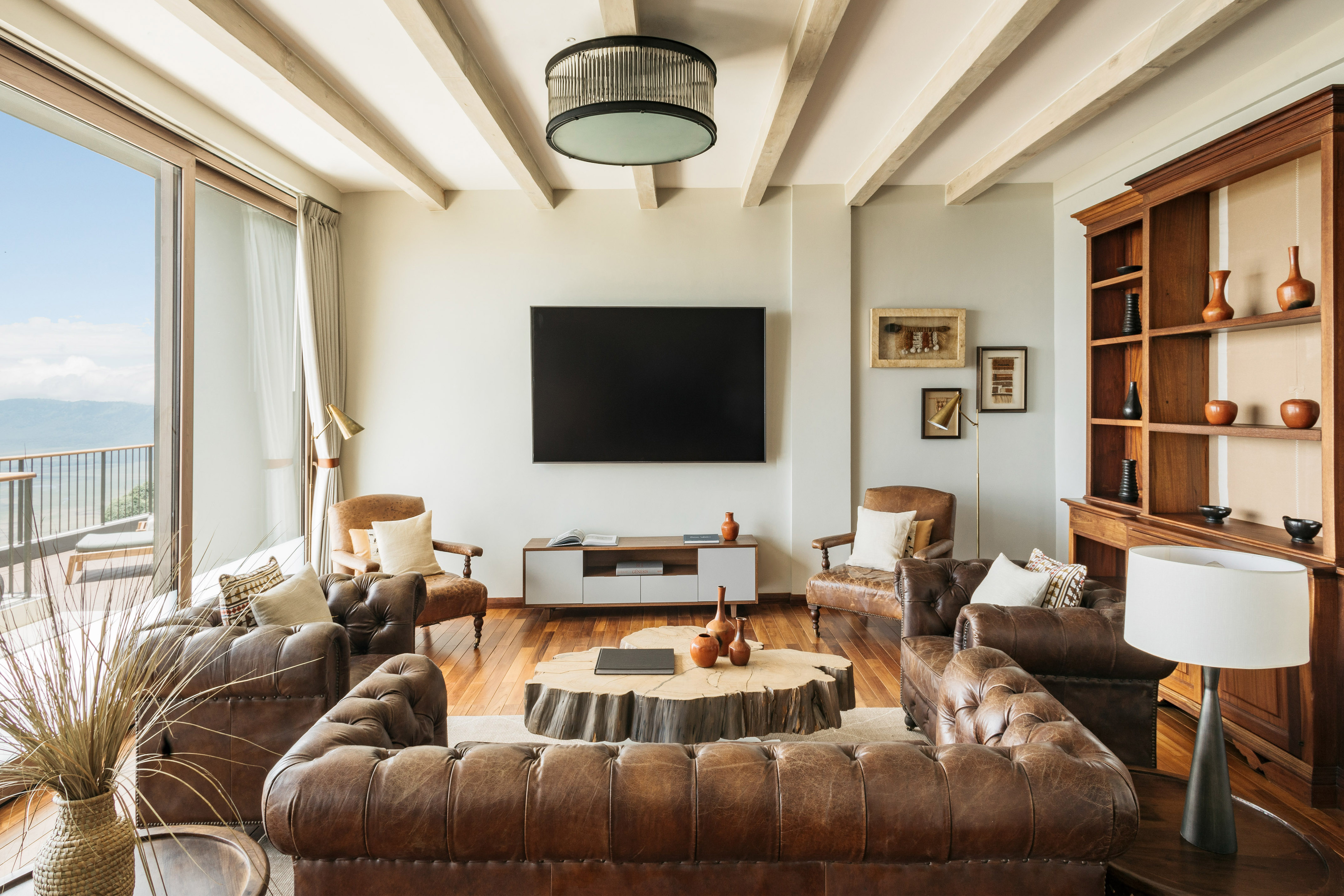 Rustic modern living room, brown leather sofas, wood coffee table, balcony view.