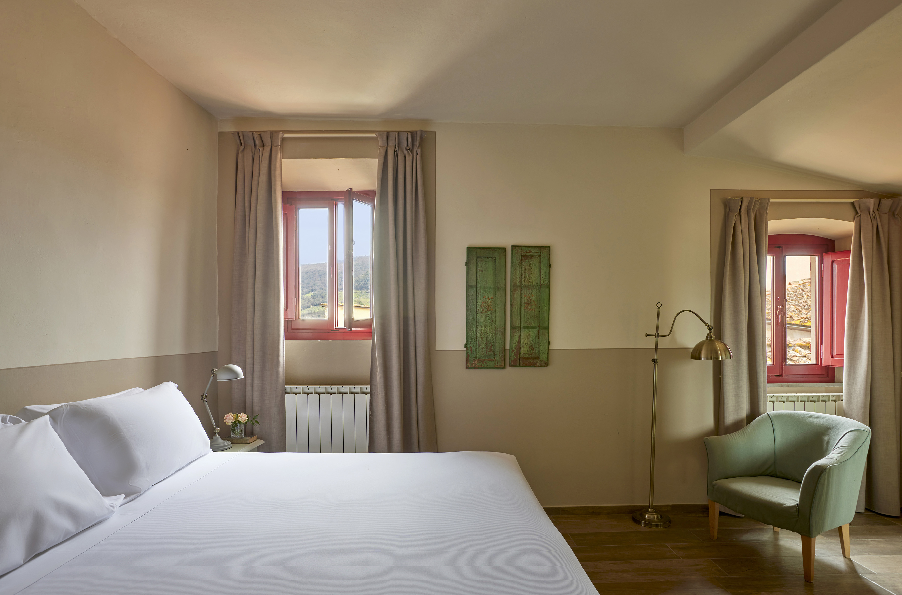 Bright rustic bedroom with white bed, open red windows, green armchair.
