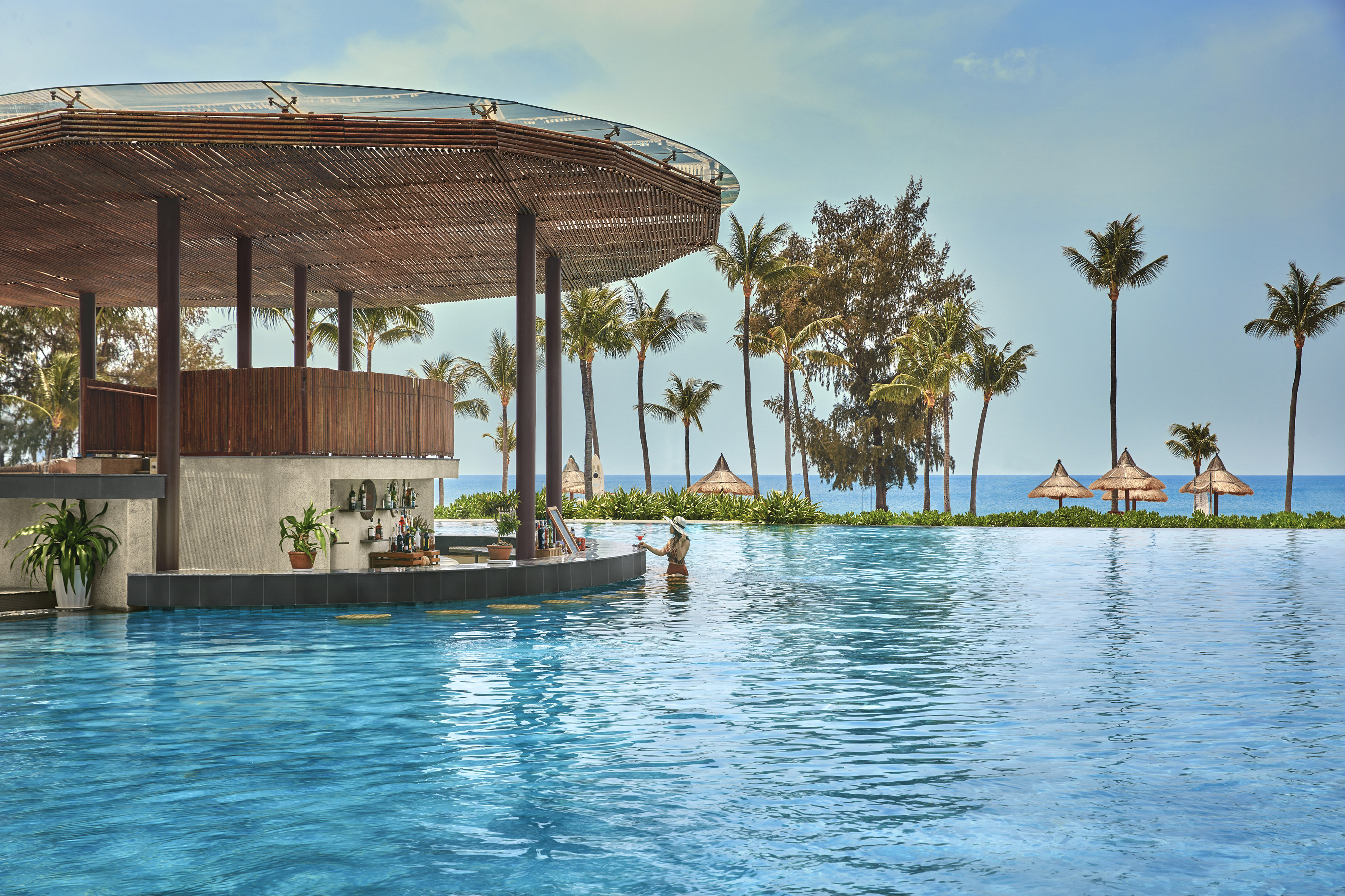 Tropical infinity pool with swim-up bar, person, palm trees, and ocean view.