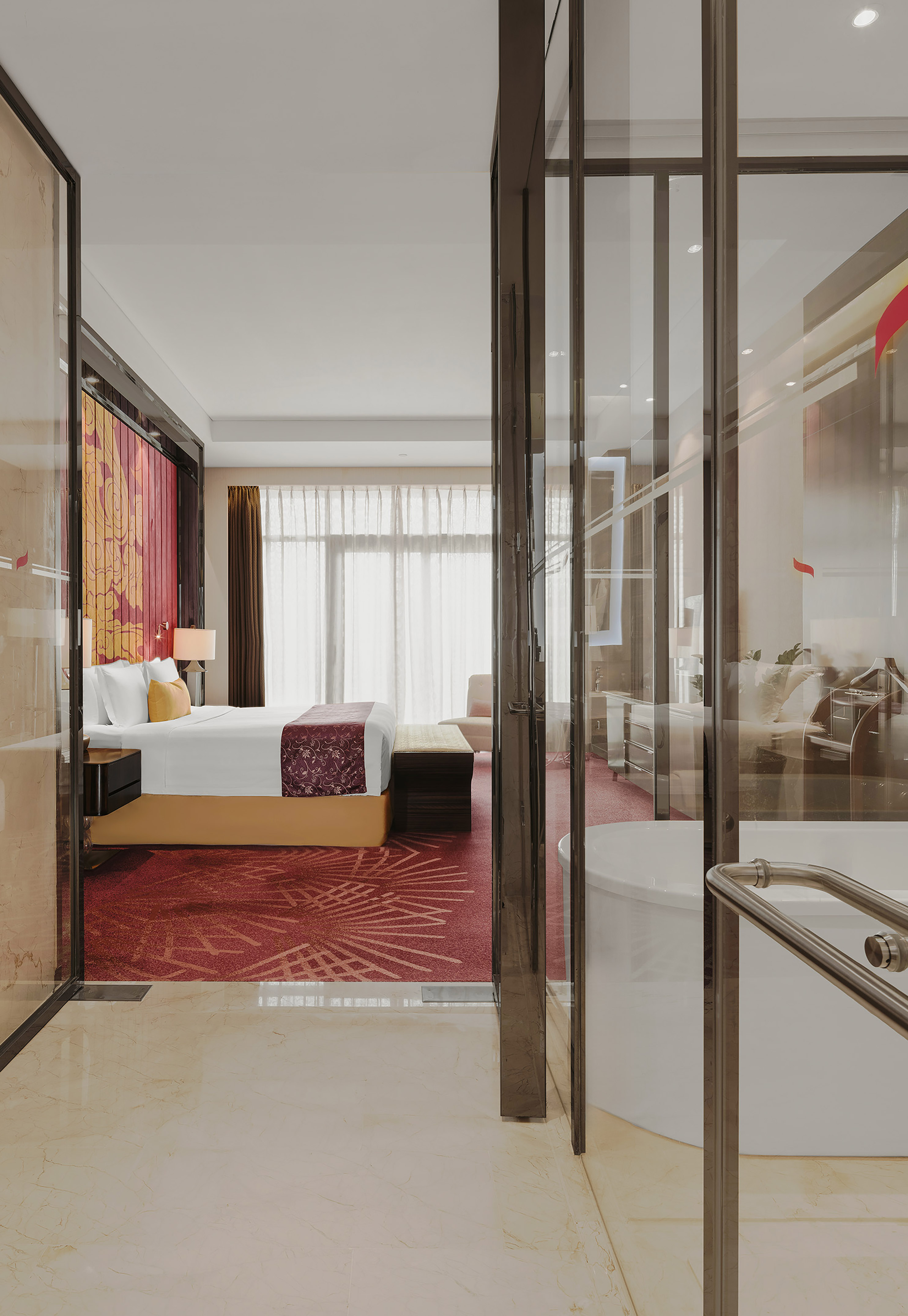 Elegant hotel bedroom and bathroom with red carpet, large bed, and bathtub.