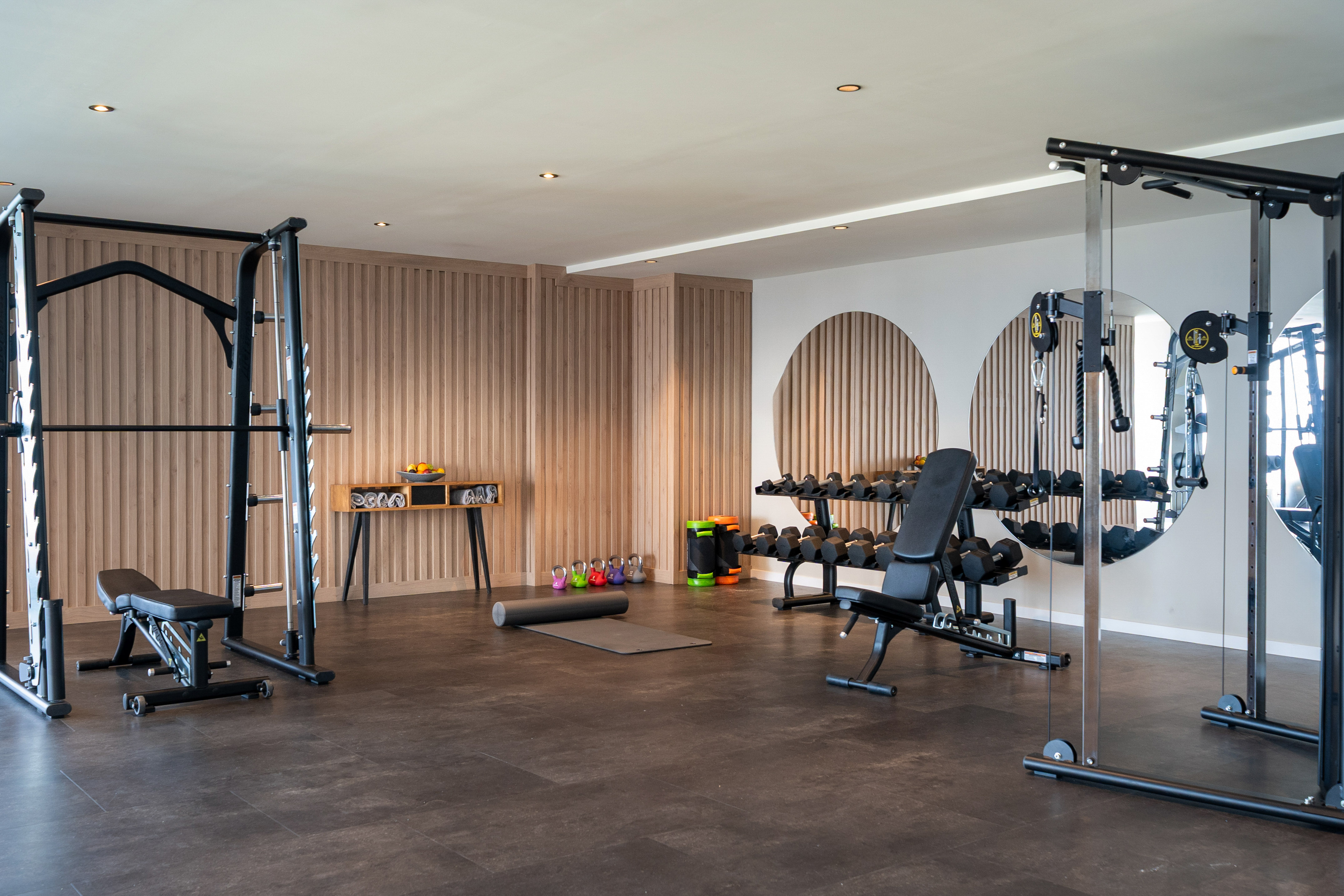 Modern gym interior with smith machine, dumbbells, kettlebells, and cable machine.