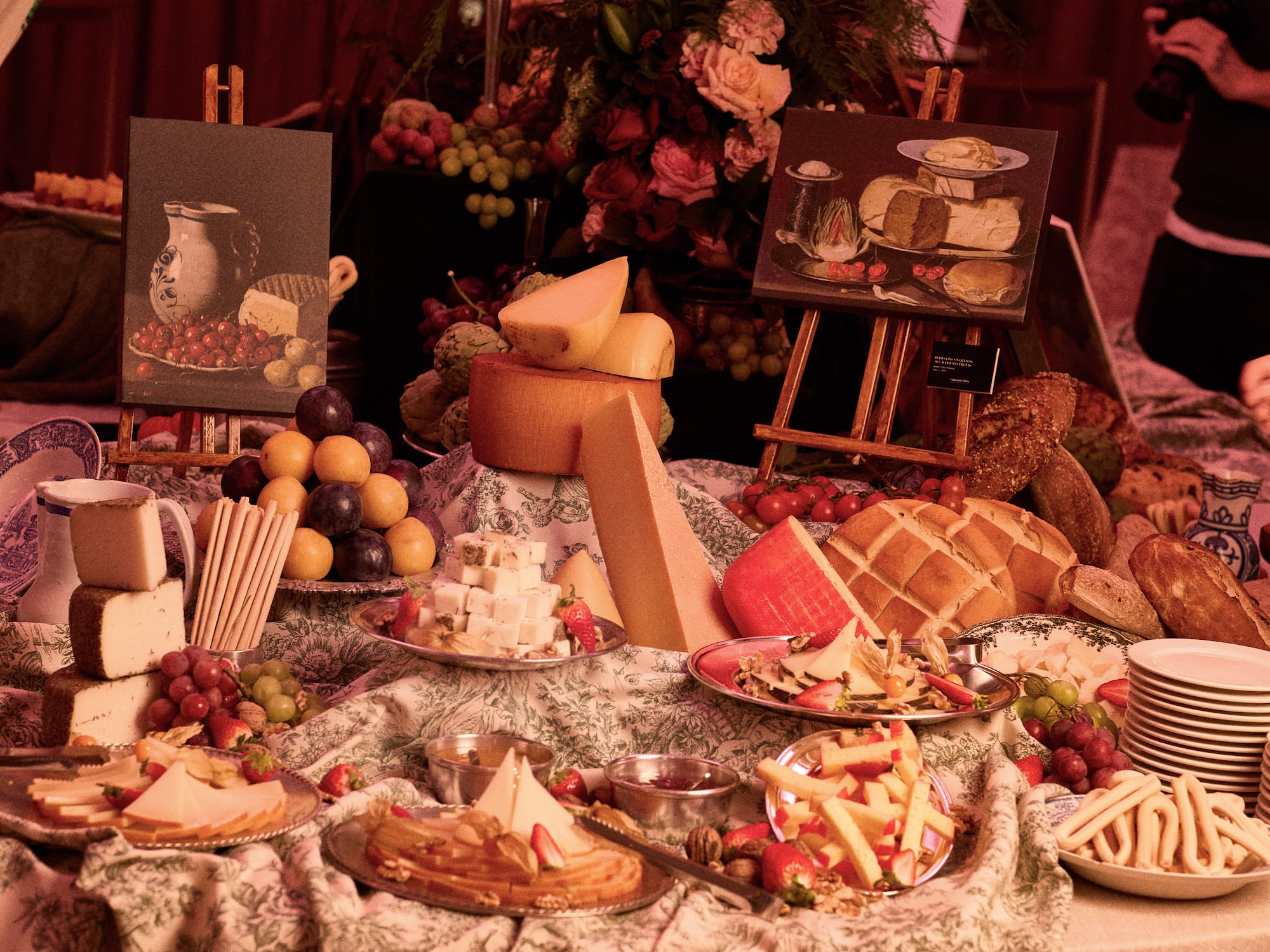 Cheese and fruit buffet with bread, crackers, and still life art.