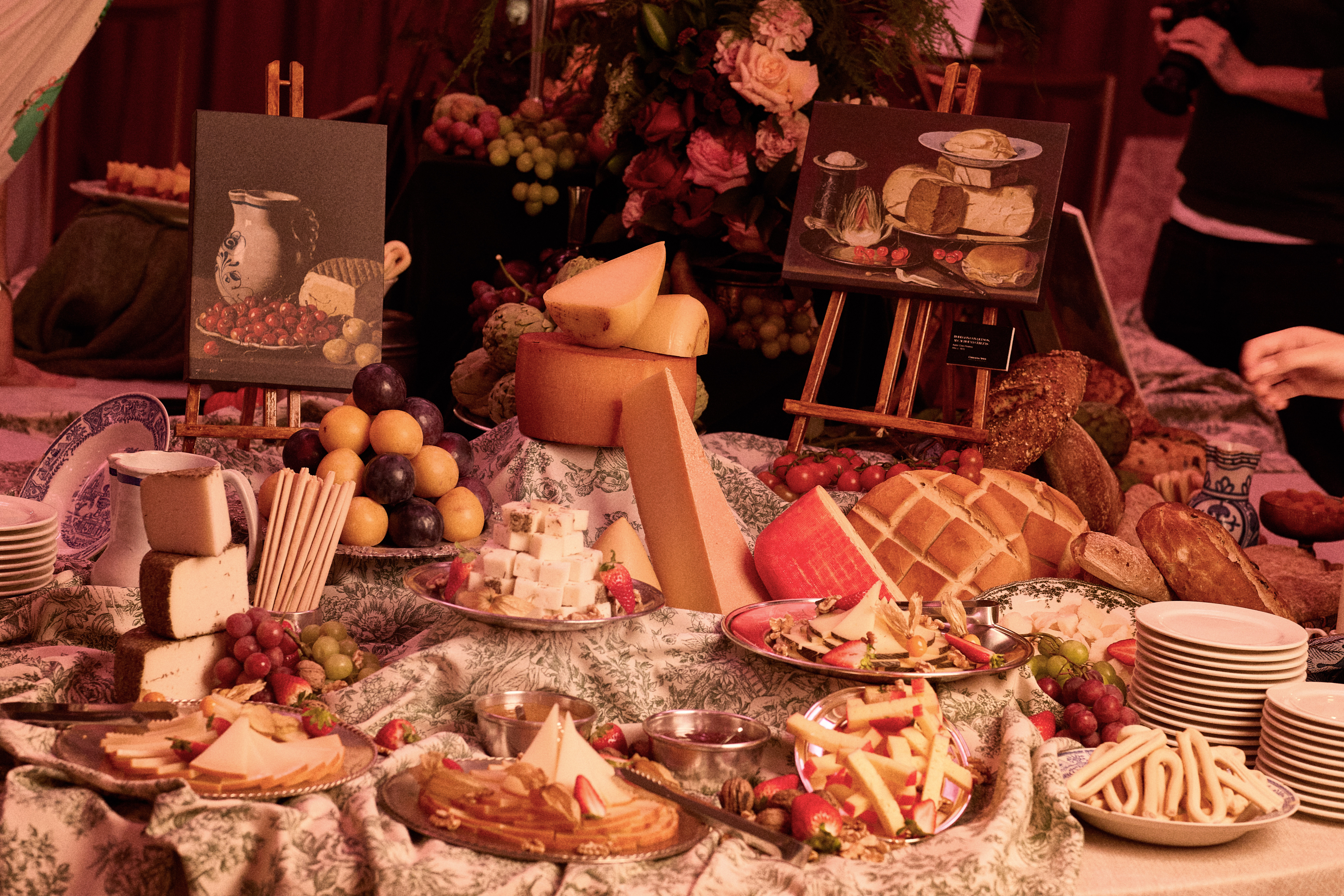 Cheese and fruit buffet with bread, crackers, and still life art.