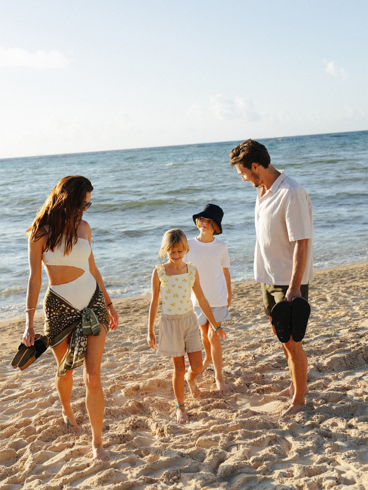 Family with two kids walking on a sandy beach by the ocean.