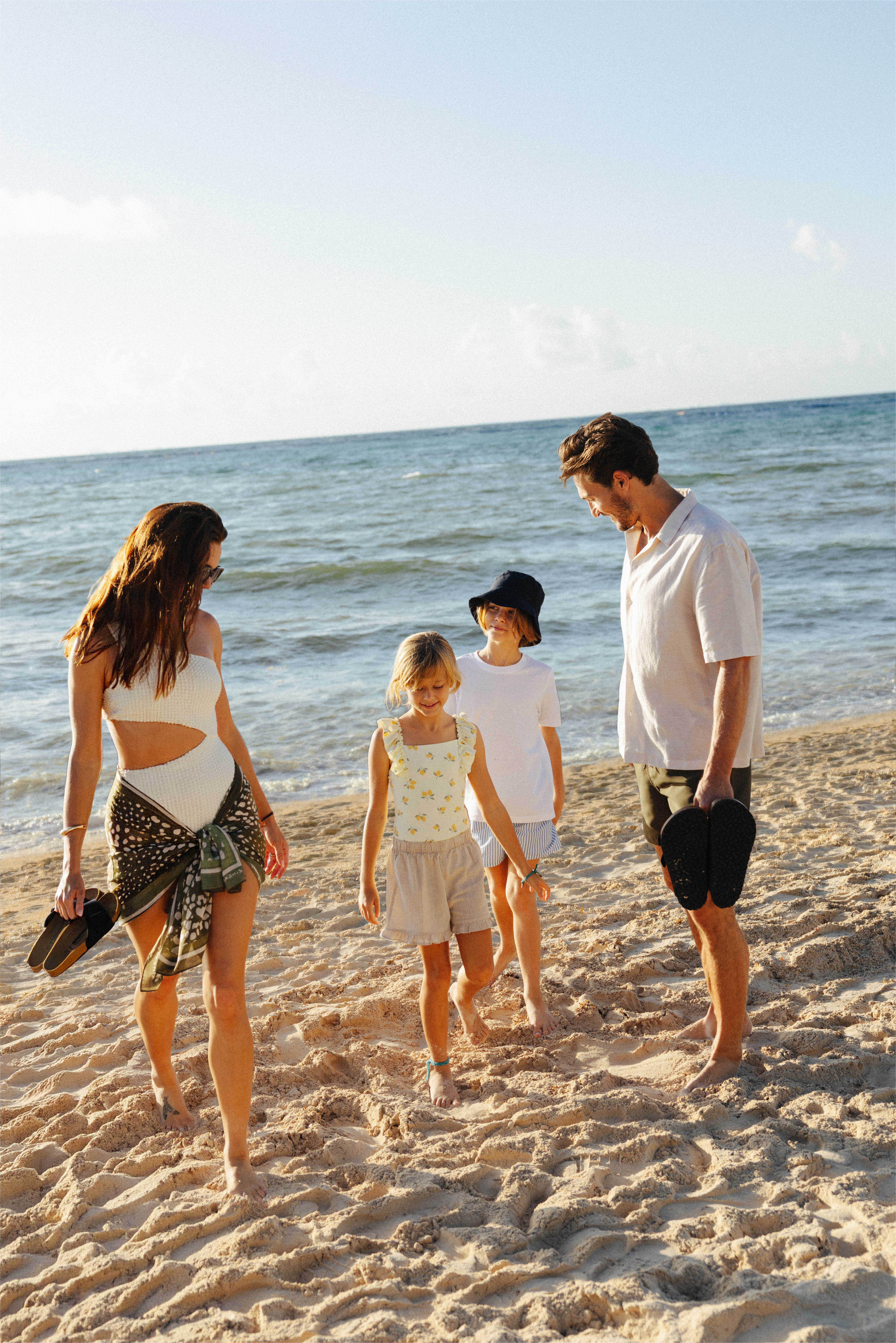 Family with two kids walking on a sandy beach by the ocean.